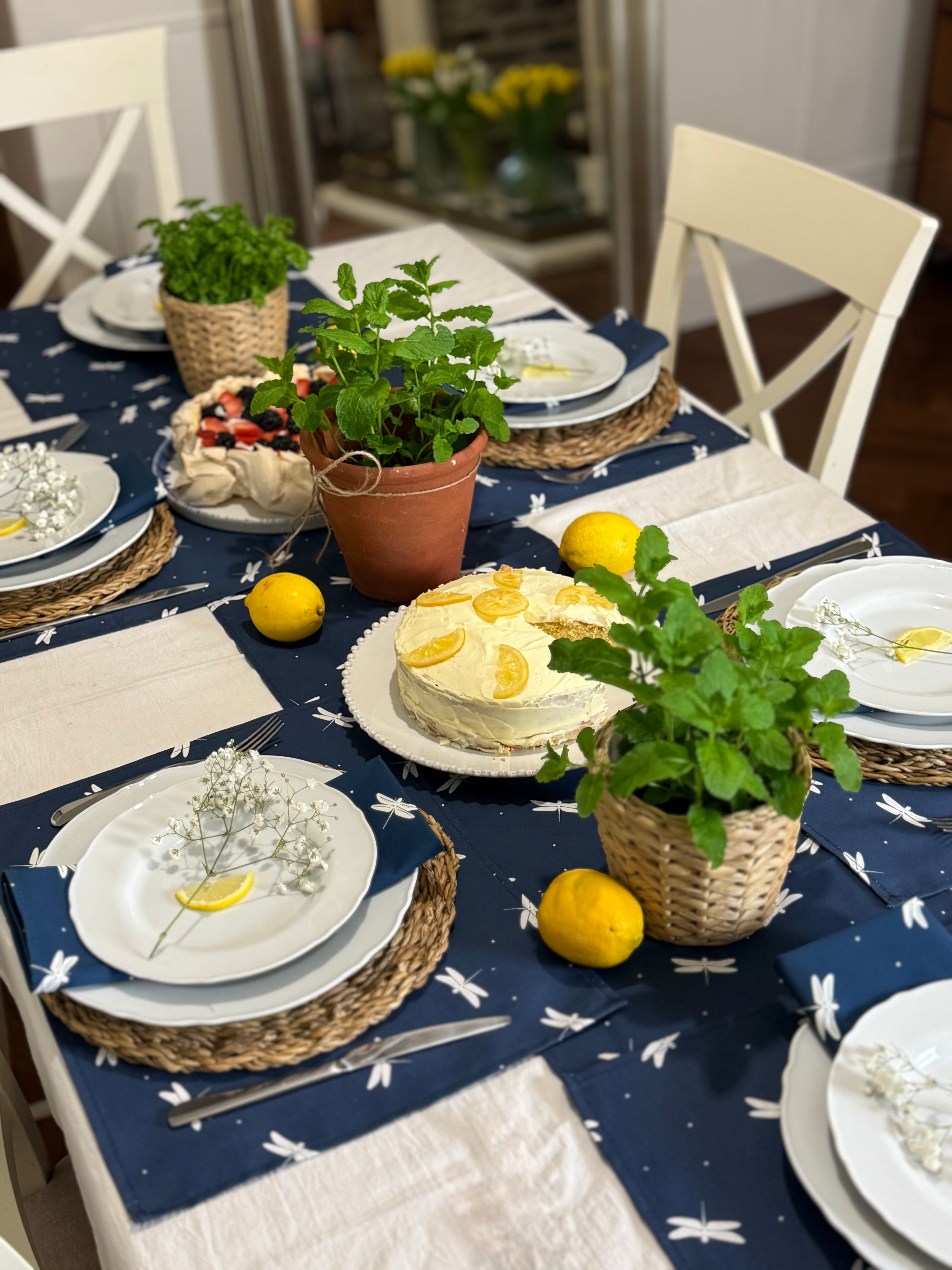 Decorative table setting with a cake, lemons, and plants on a navy blue dragonfly design table runner