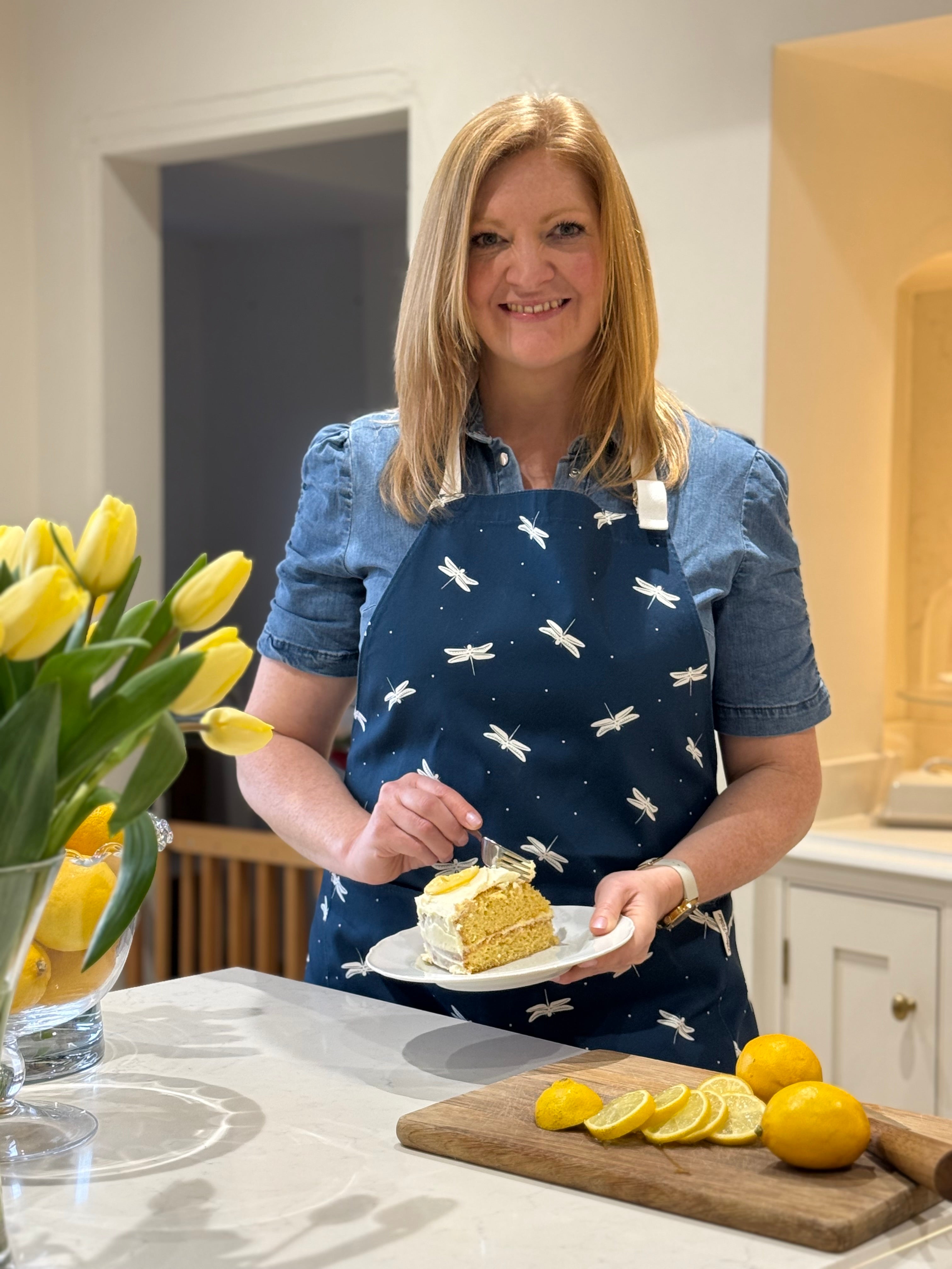 Rebecca Pitcher wearing a navy apron with dragonfly pattern eating a slice of lemon cake