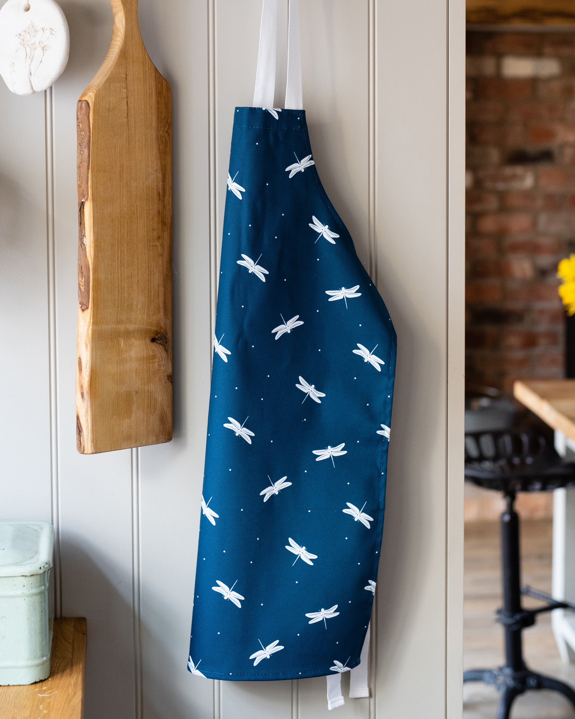 Blue children's apron with white dragonfly pattern hanging on a kitchen wall