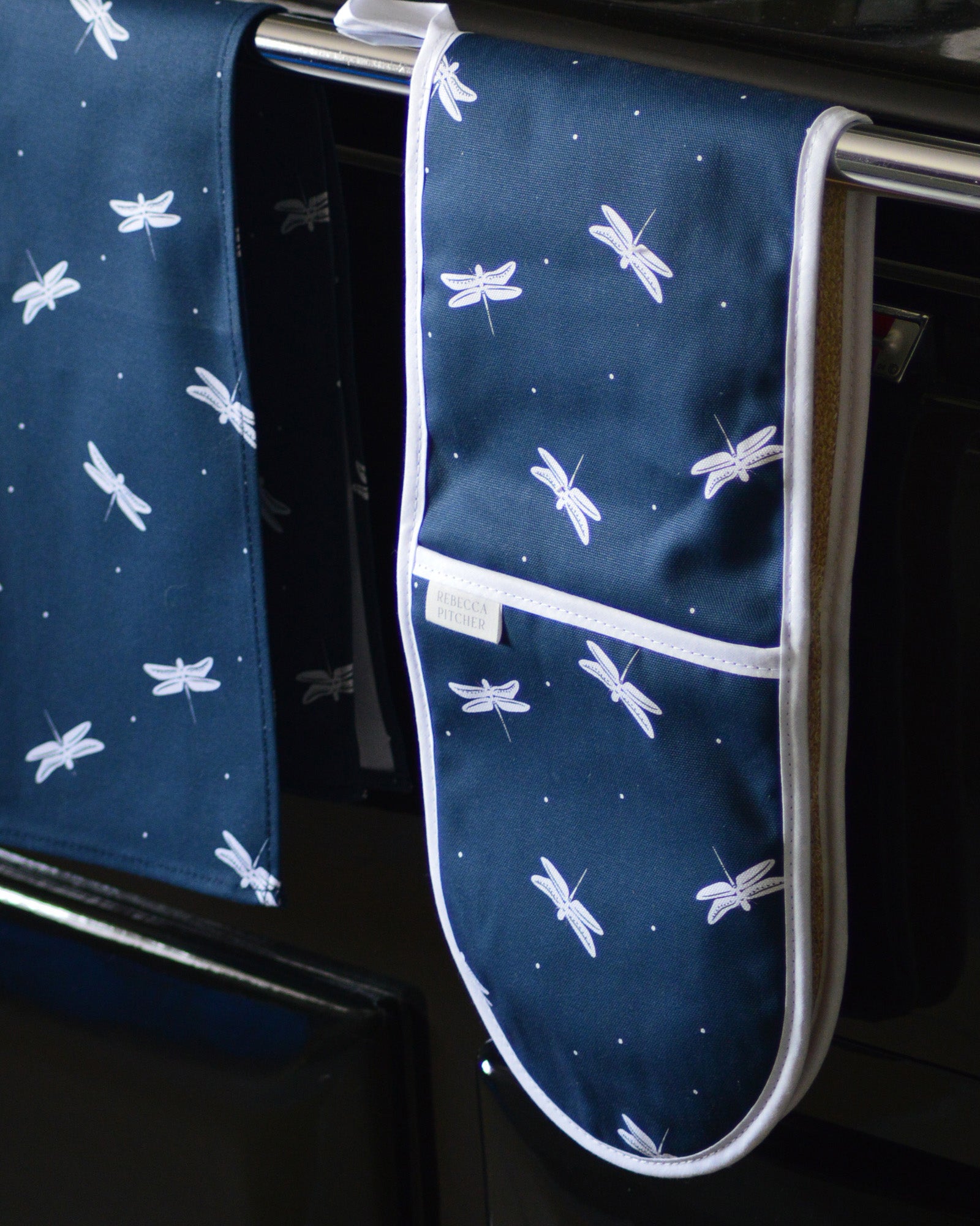 Blue oven mitt with white dragonfly pattern hanging on a range cooker