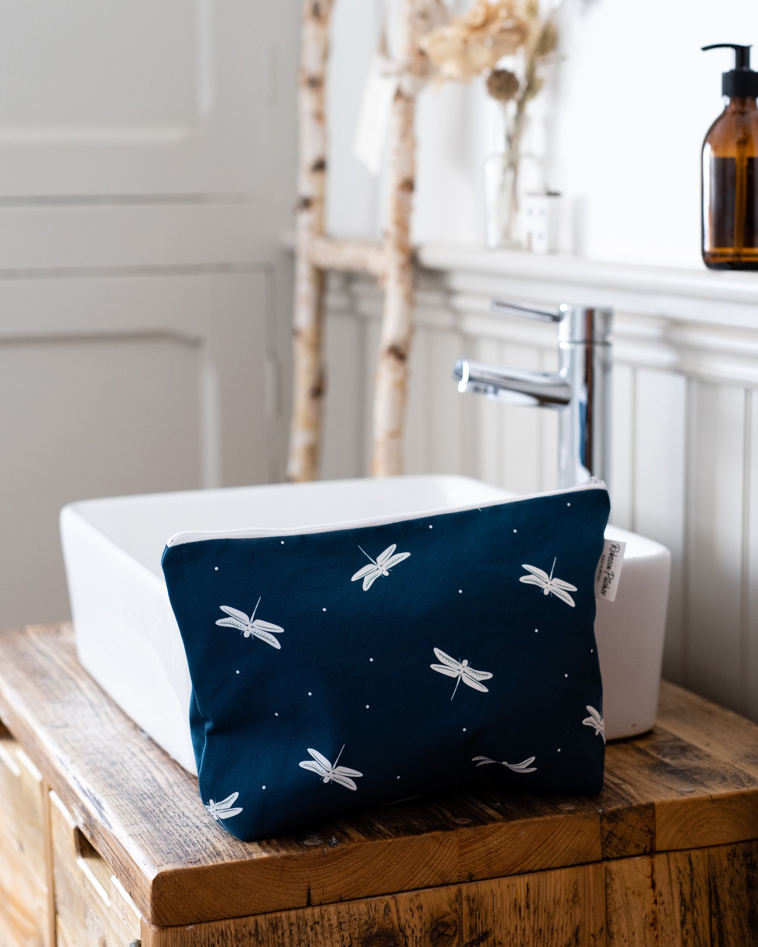 Navy pouch with white dragonfly patterns on a wooden surface next to a sink.