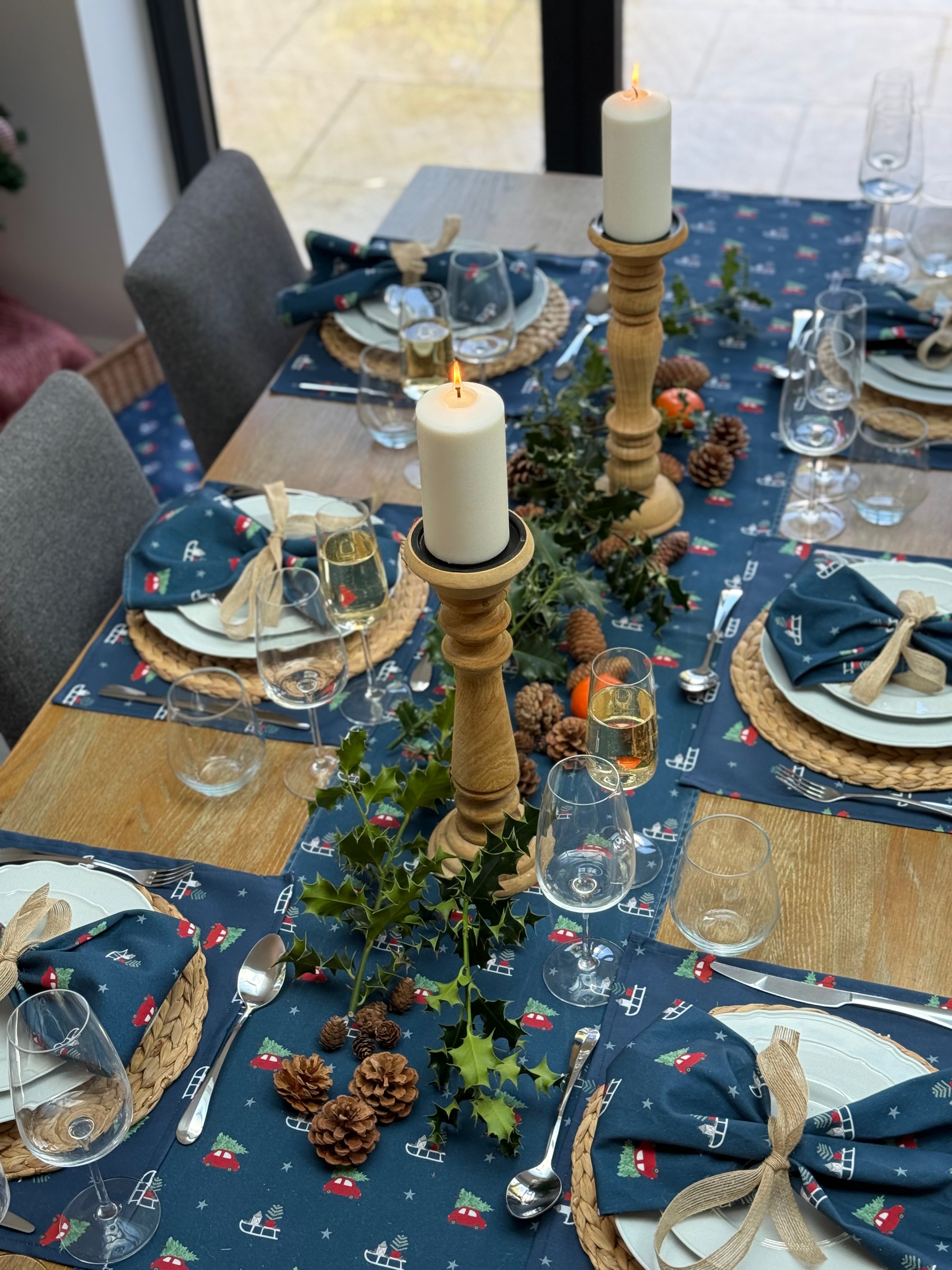 Rustic Christmas table setting with candles, glasses, and decorative elements on a blue Christmas table runner