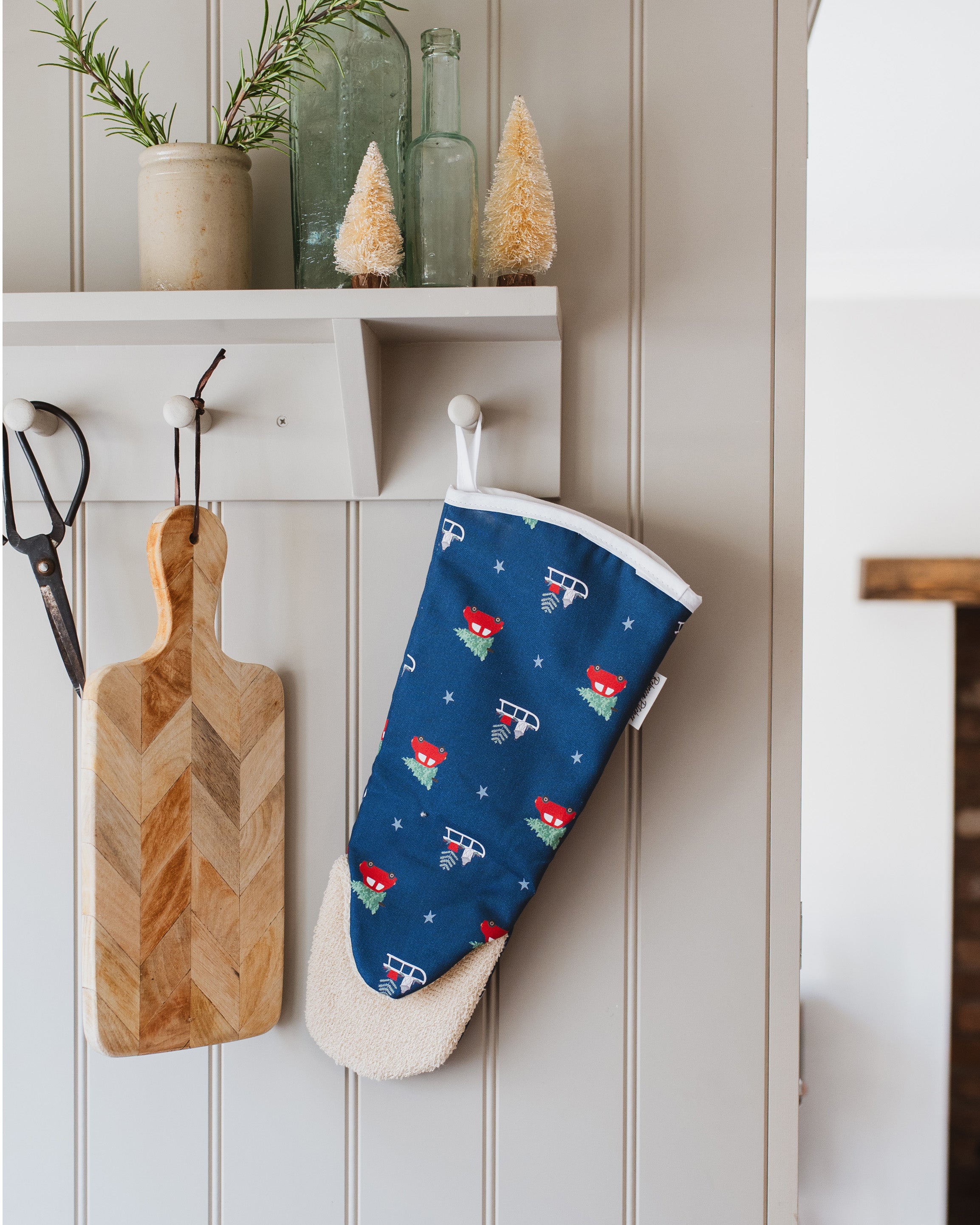 Navy blue oven mitt with red and white Christmas pattern hanging on a white wall next to a wooden cutting board.