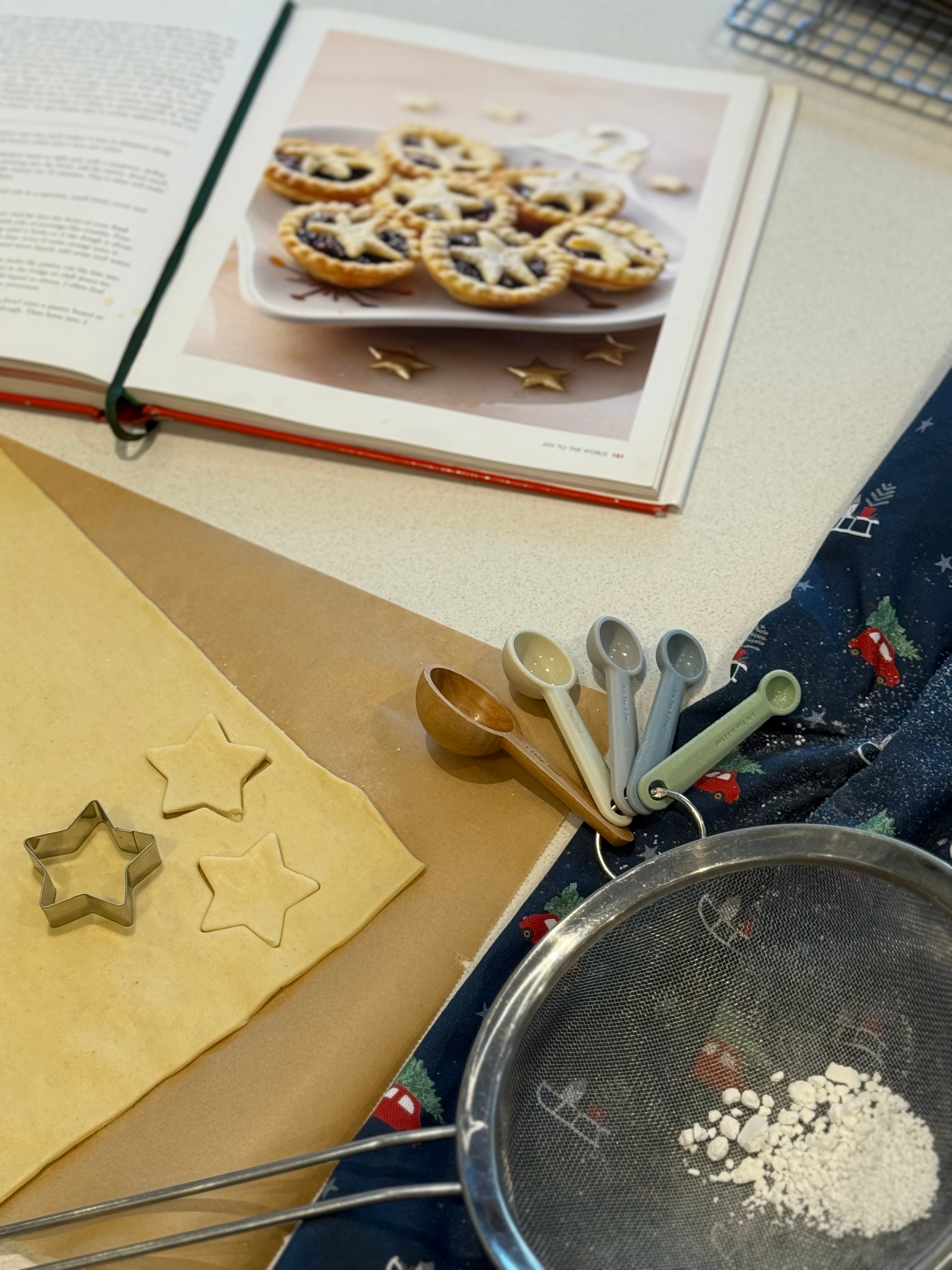 Baking setup with cookie dough, cutters, and a cookbook resting on a Christmas tea towel