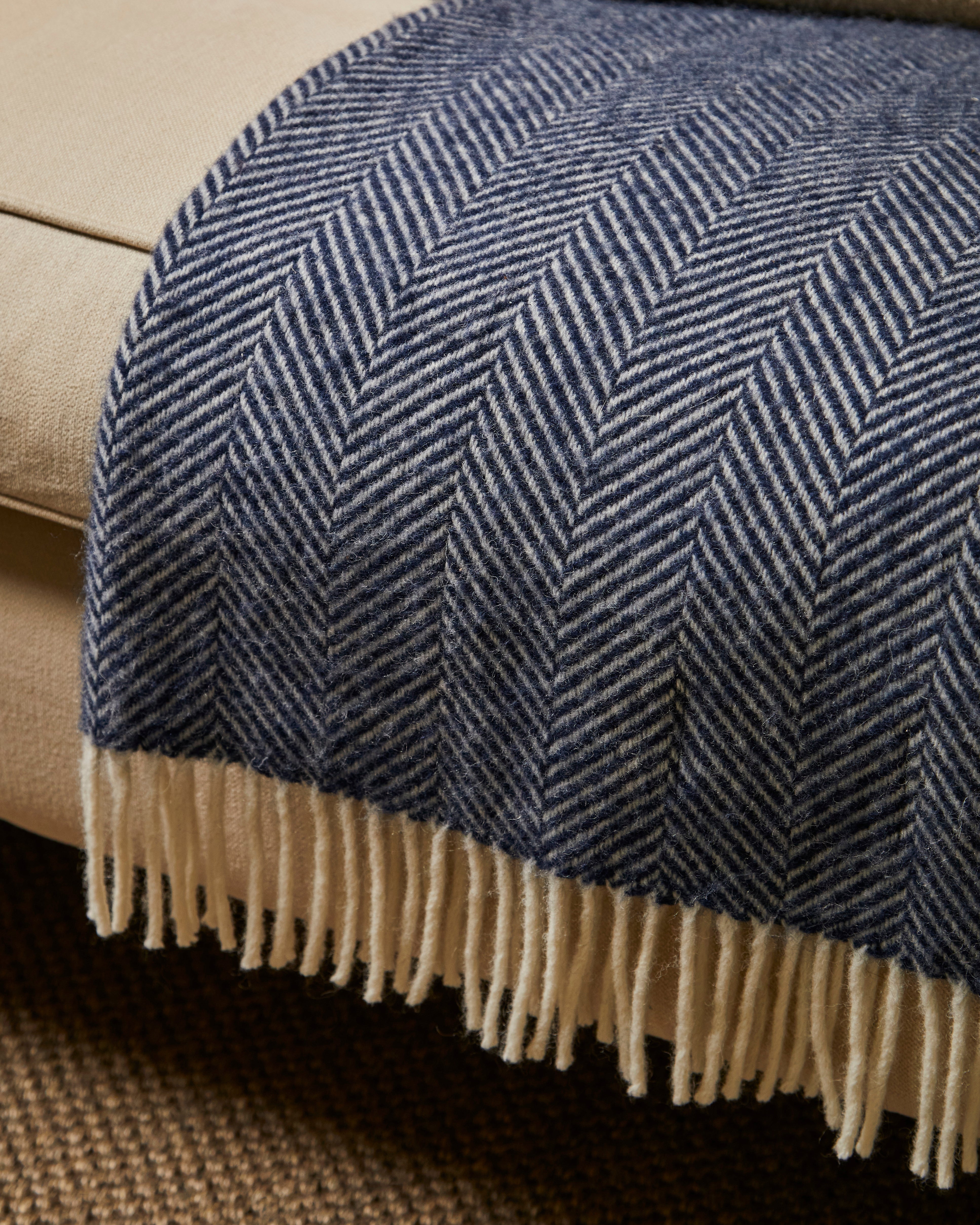 Blue herringbone patterned throw blanket with beige fringe on a beige couch.