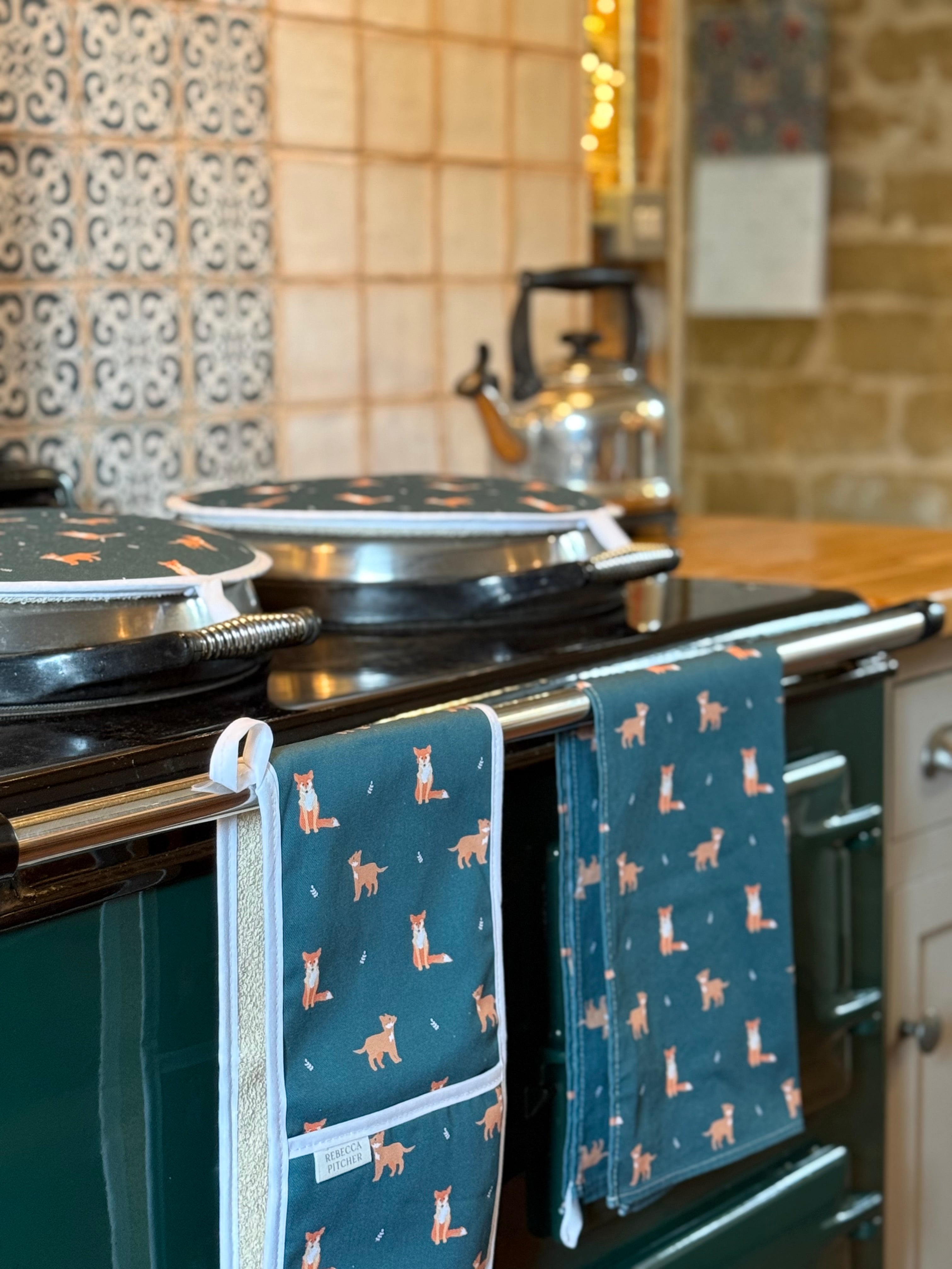 Kitchen scene with a stove and dark green towels with fox patterns hanging on it.
