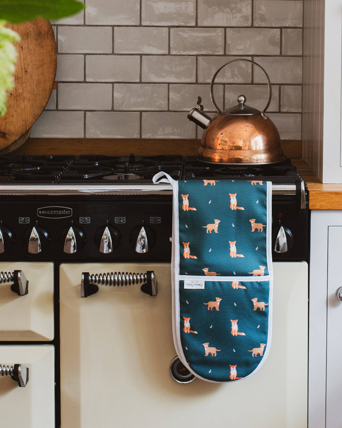 Dark Green Oven mitt with fox pattern hanging on a kitchen stove