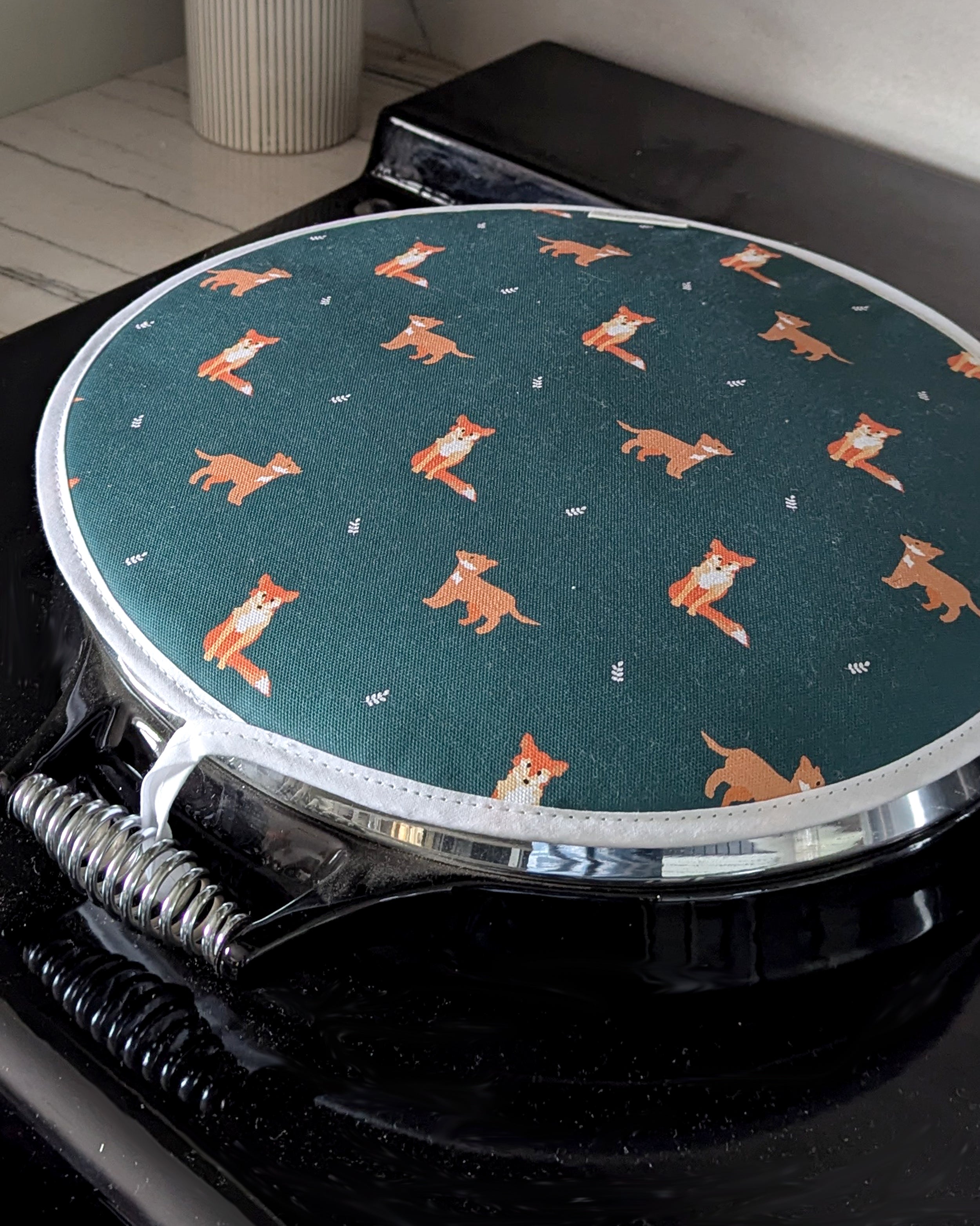 Round dark green hob cover with fox pattern on a black range cooker