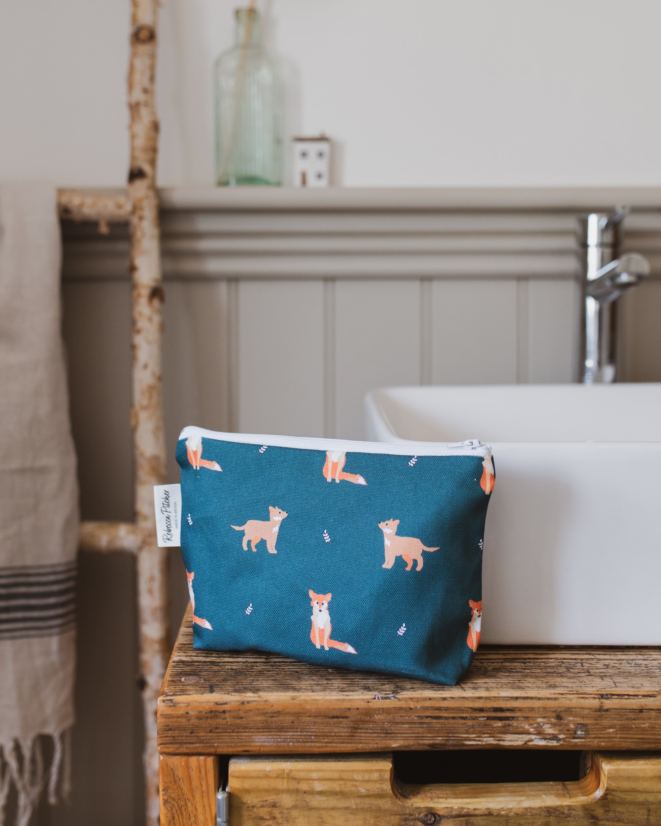Green pouch with fox pattern on a wooden surface in a bathroom setting