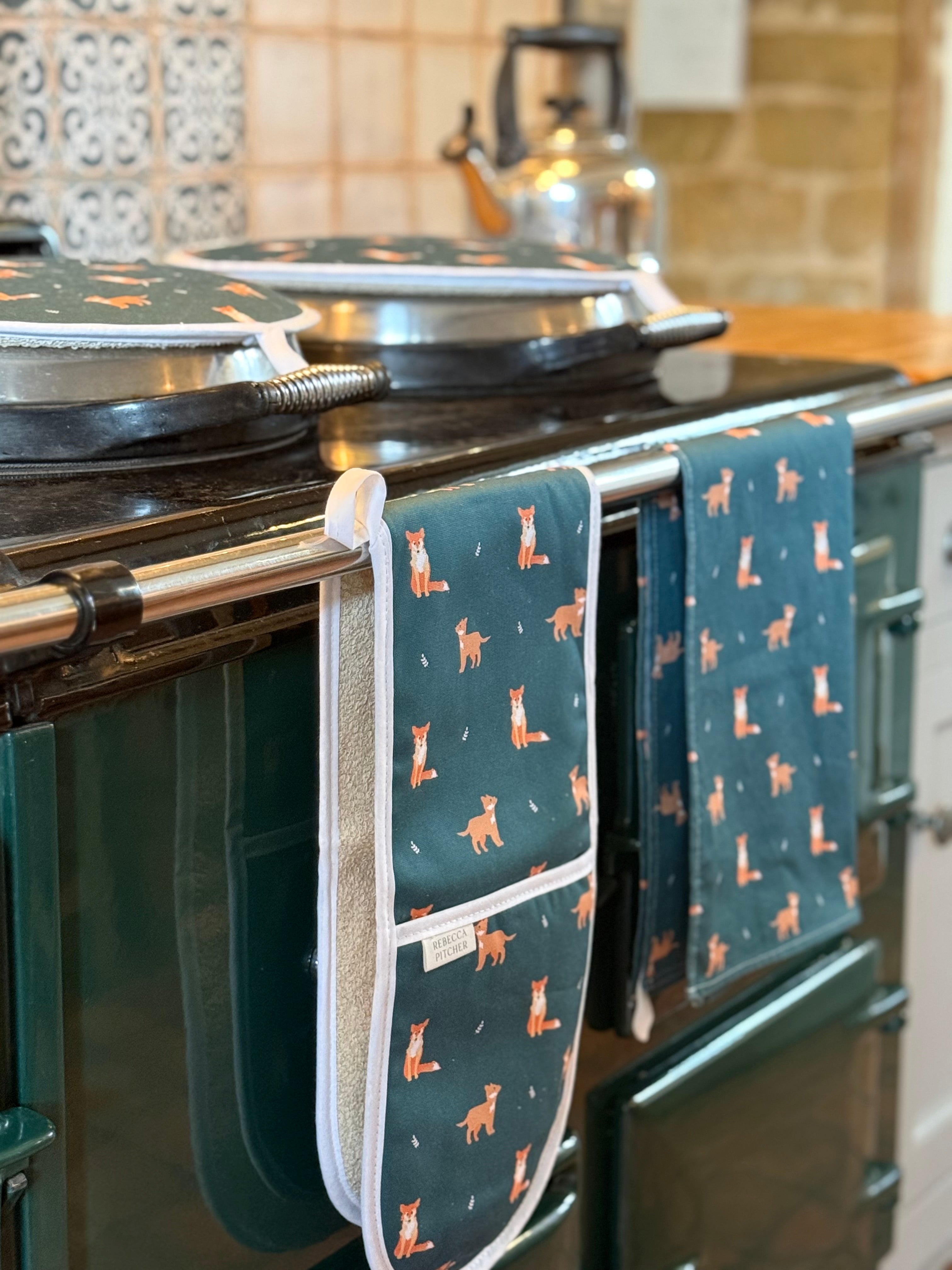 green oven mitts with fox pattern hanging on a stove in a kitchen.