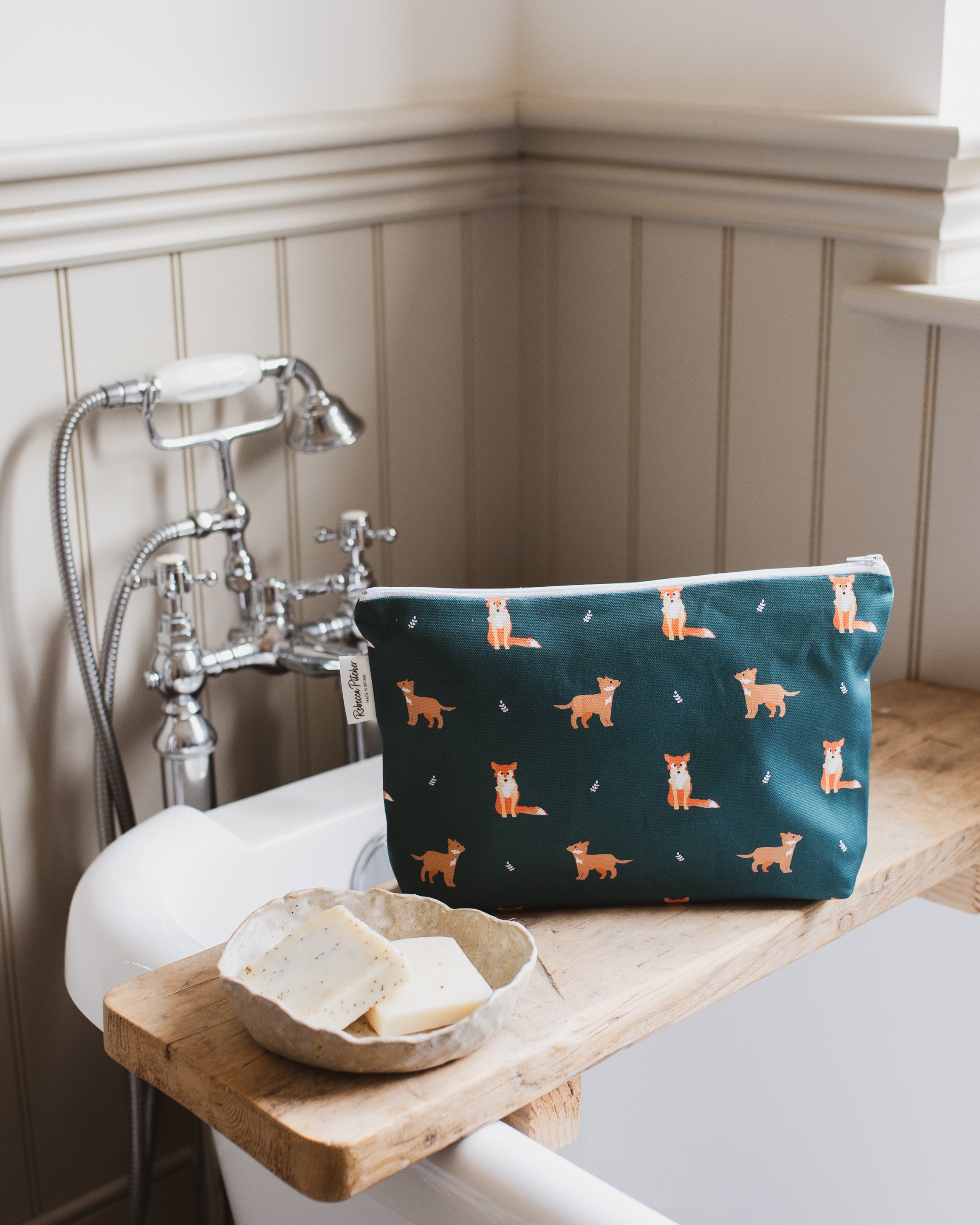Green washbag with fox pattern on a bathroom shelf next to soap and a wooden bowl.
