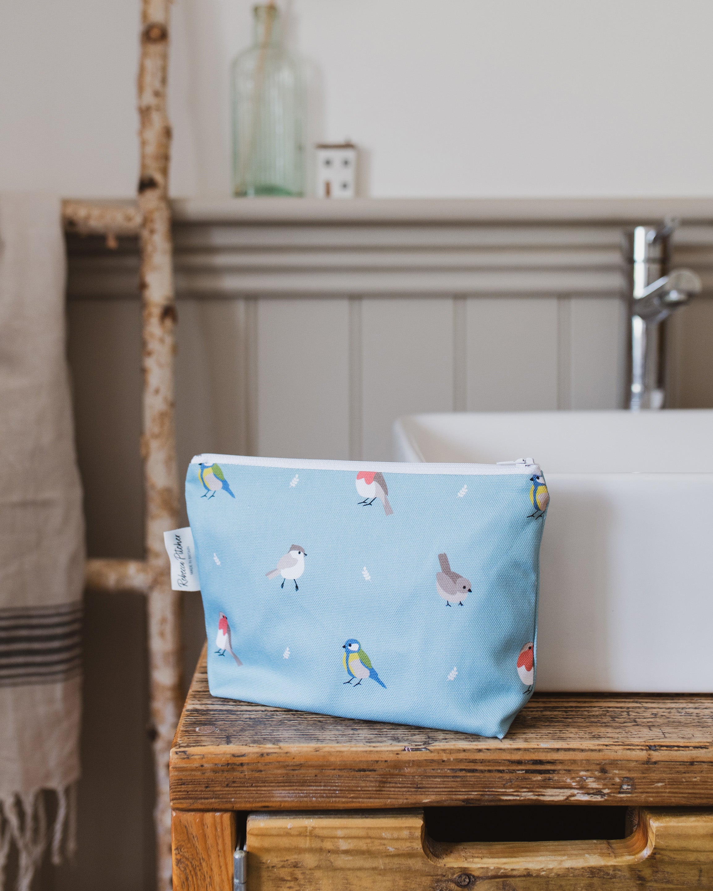 Blue makeup bag with bird design on a wooden bathroom vanity