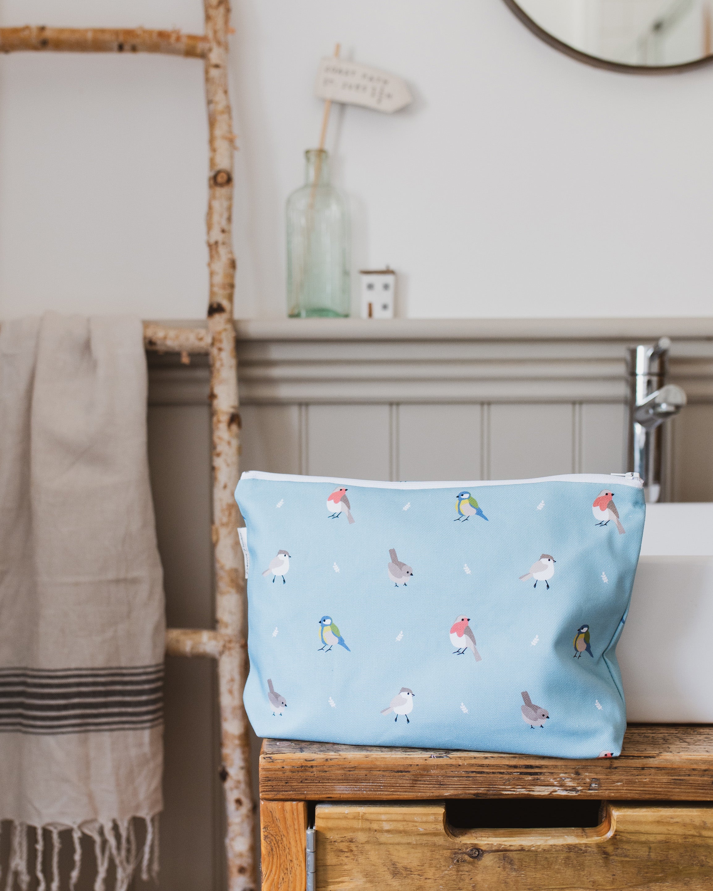 Blue washbag with bird pattern on a wooden shelf in a bathroom setting
