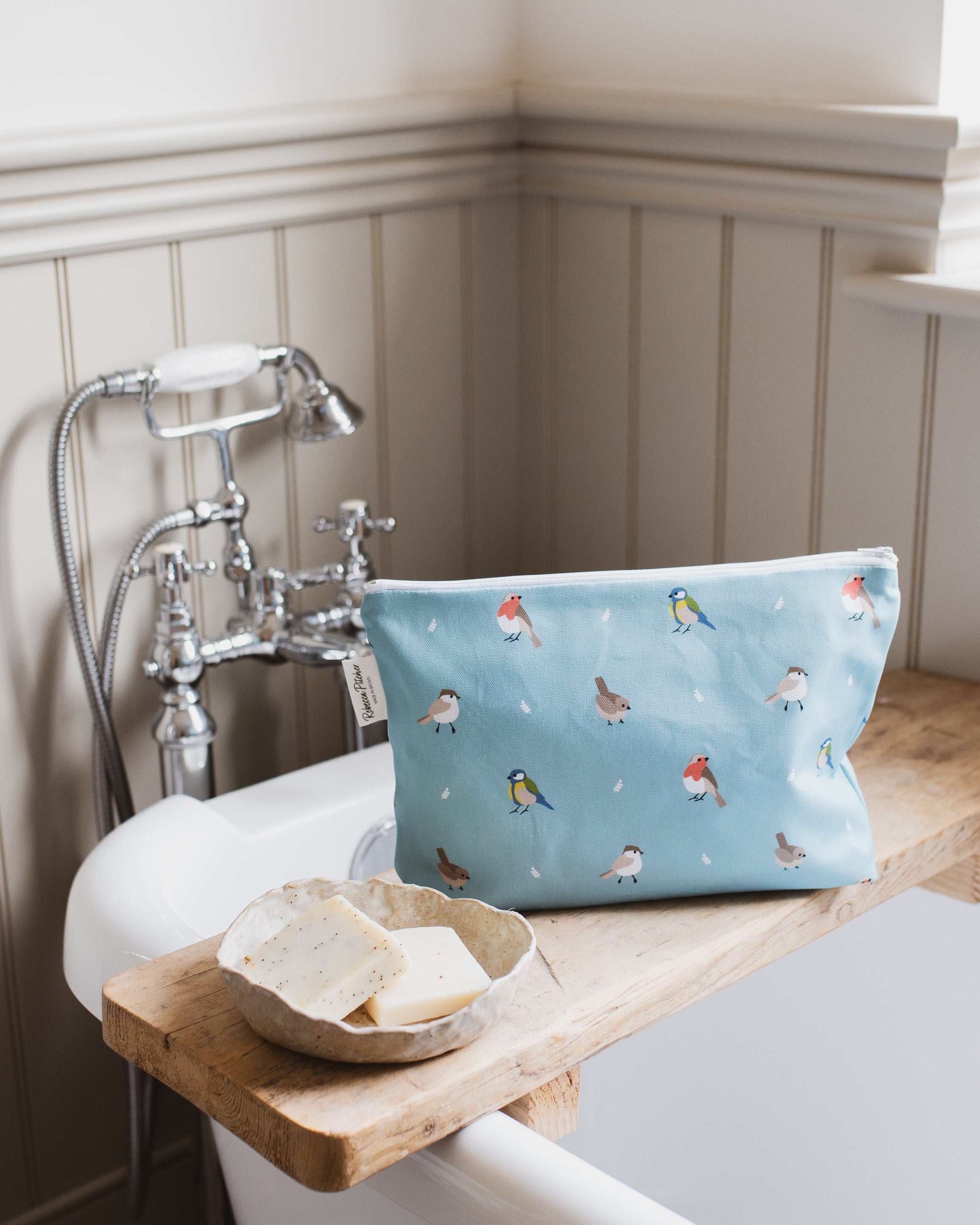Blue washbag with bird pattern on a wooden shelf in a bathroom setting