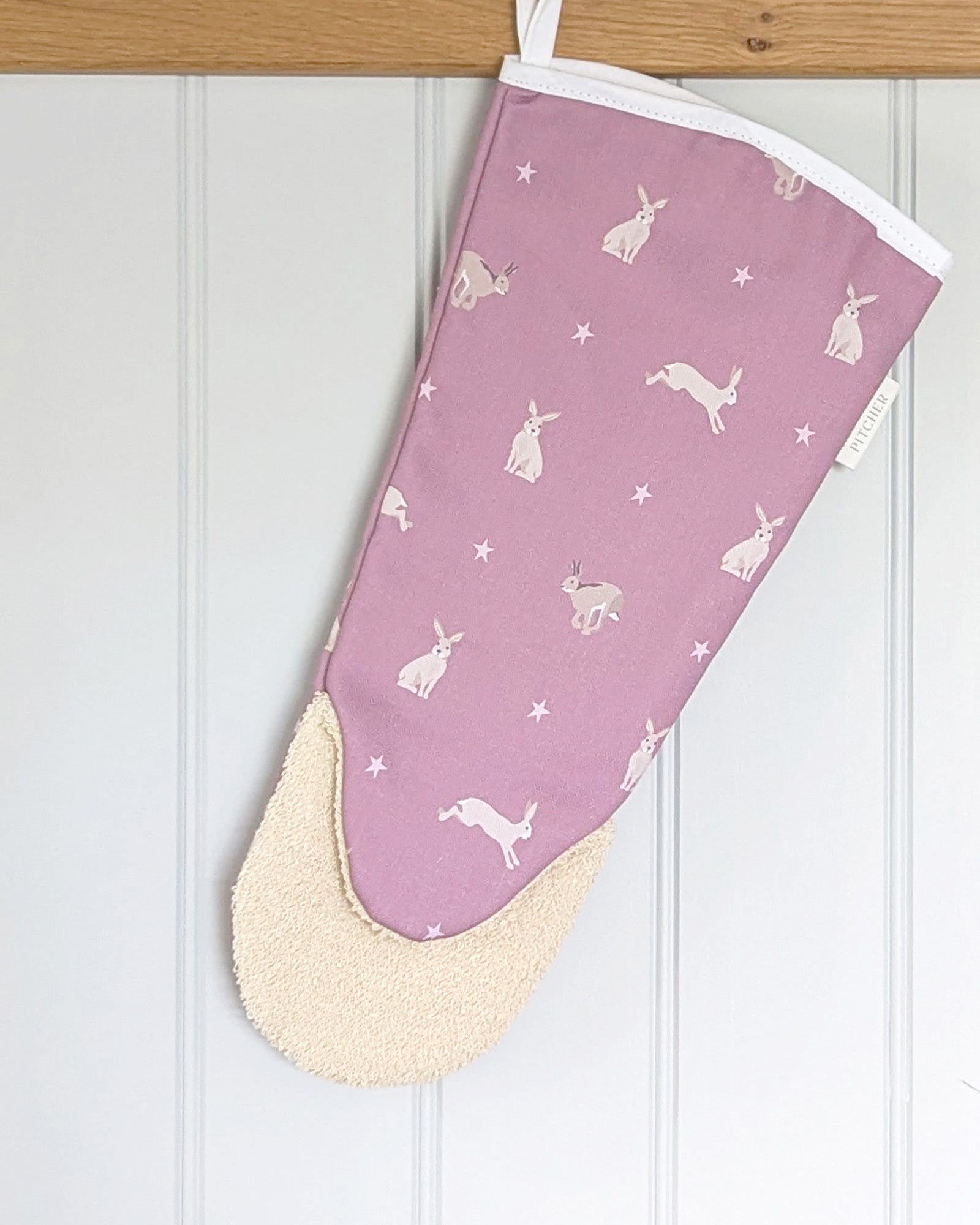 Pink oven gauntlet with hare patterns hanging on a wooden kitchen rail