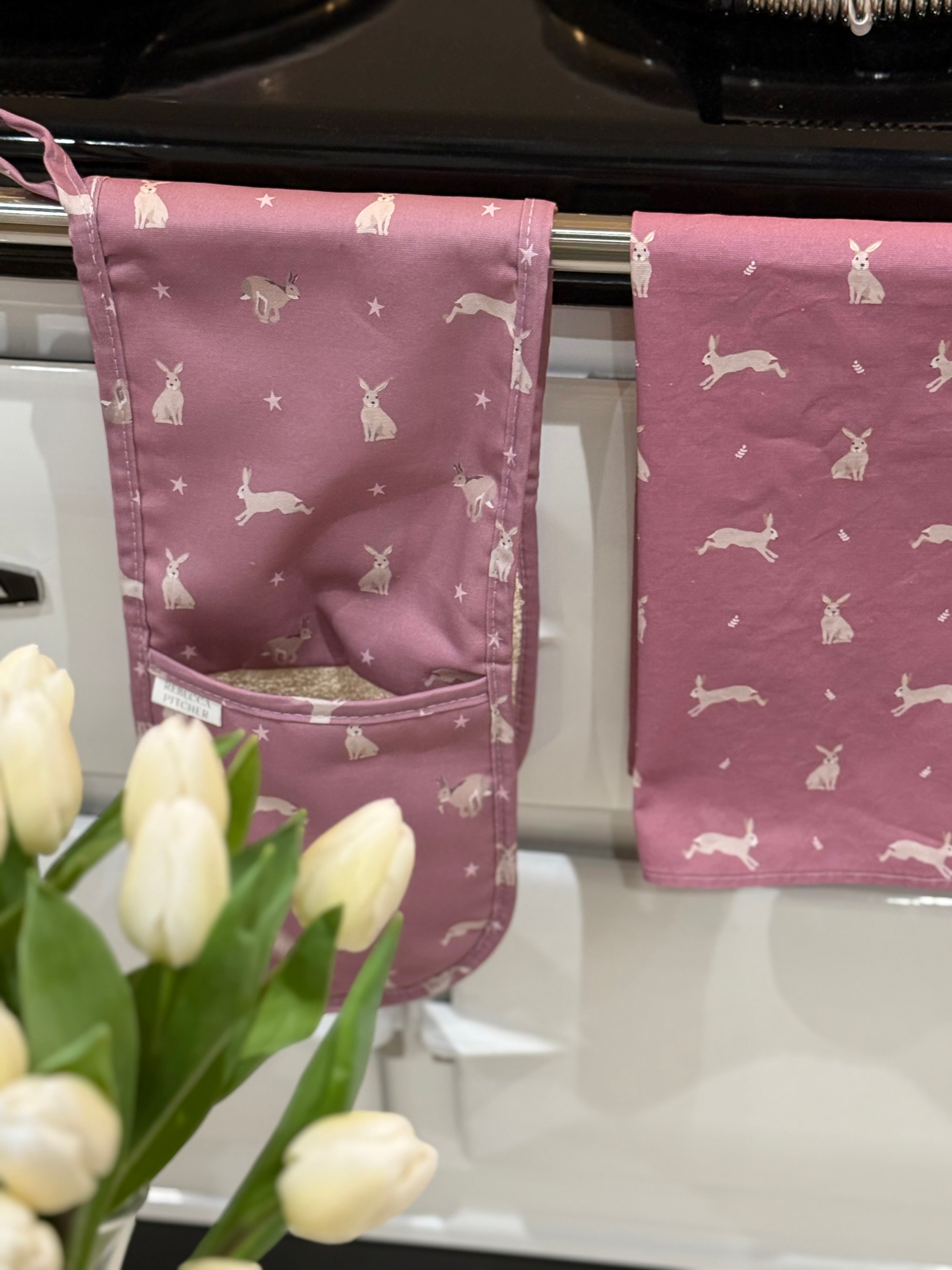 Pink hare pattern oven gloves and tea towel hanging on a cooker rail