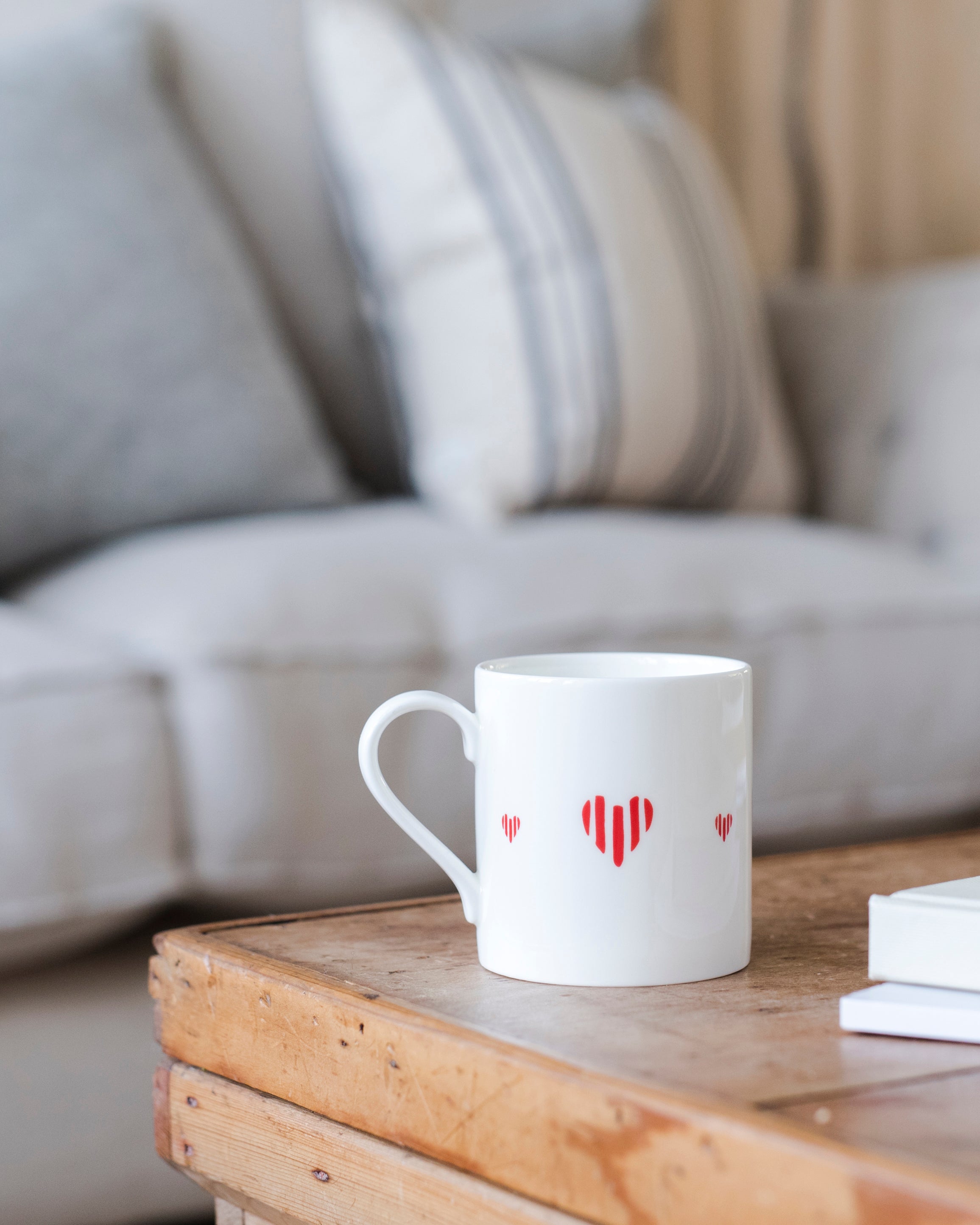 White mug with red heart design on a wooden table in a living room setting