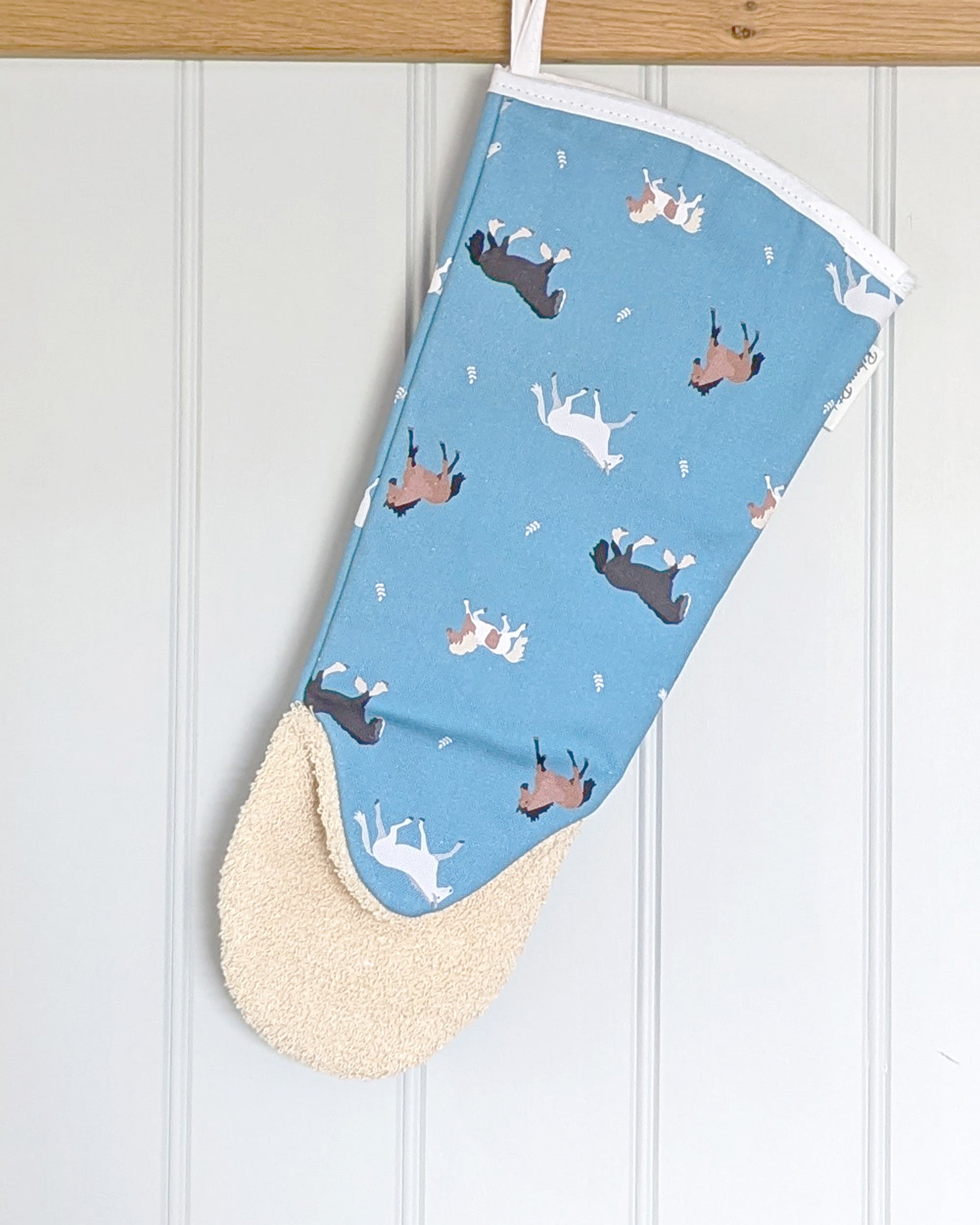 Blue long oven gauntlet with horse pattern hanging on a wooden rail