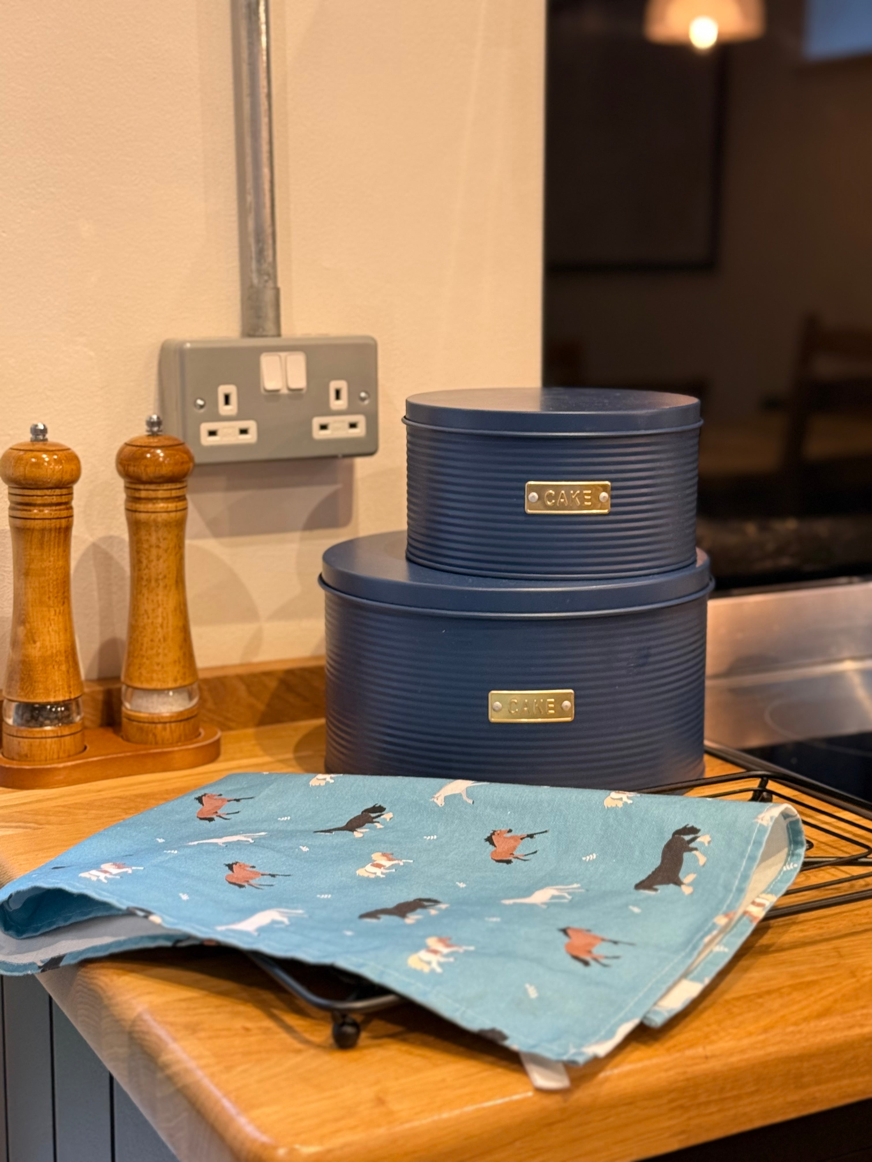 Blue cake tins on a kitchen counter with a horse patterned tea towel in front