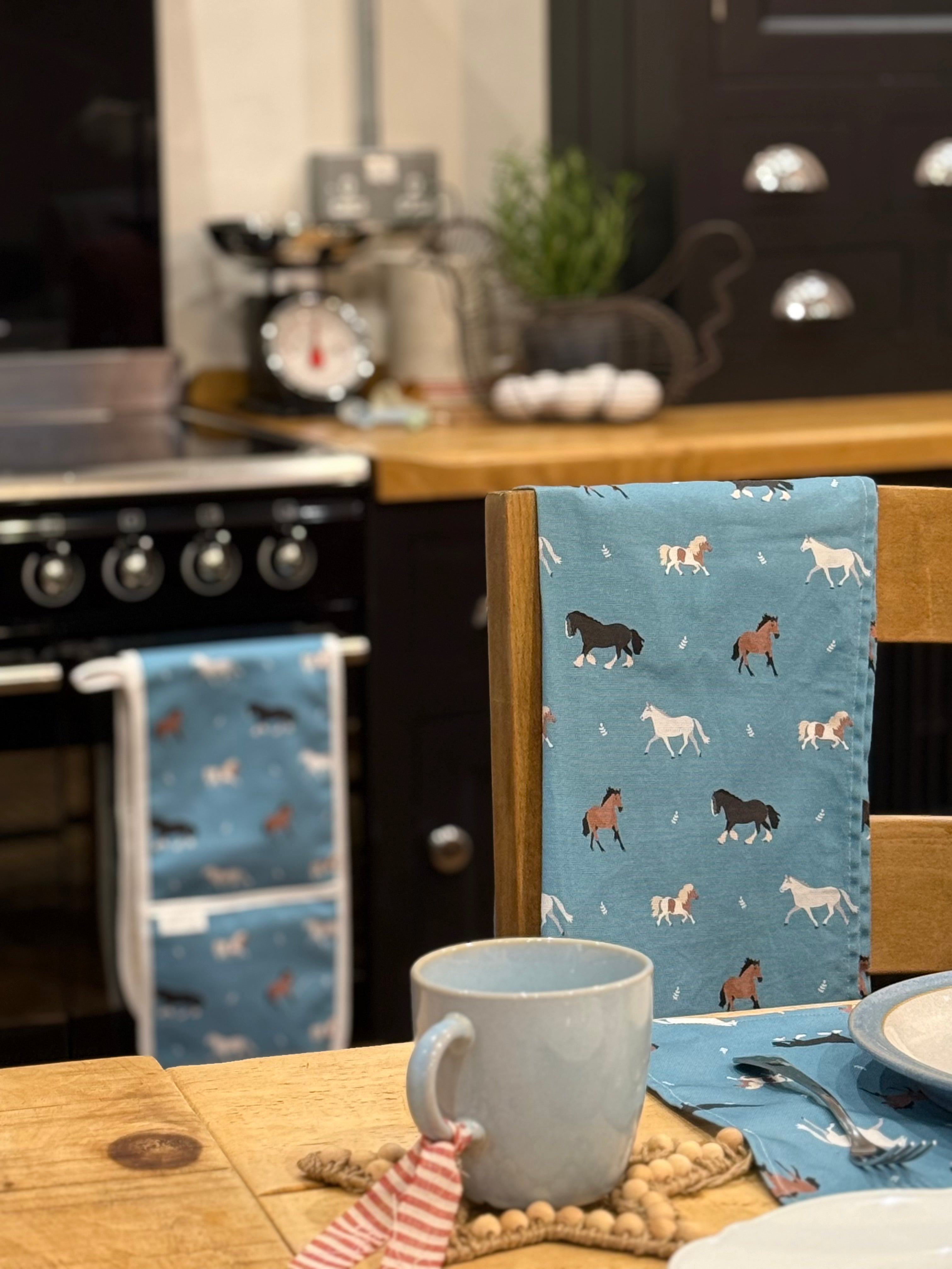 Kitchen scene with a blue tea towel featuring horse patterns, a mug, and a plate.