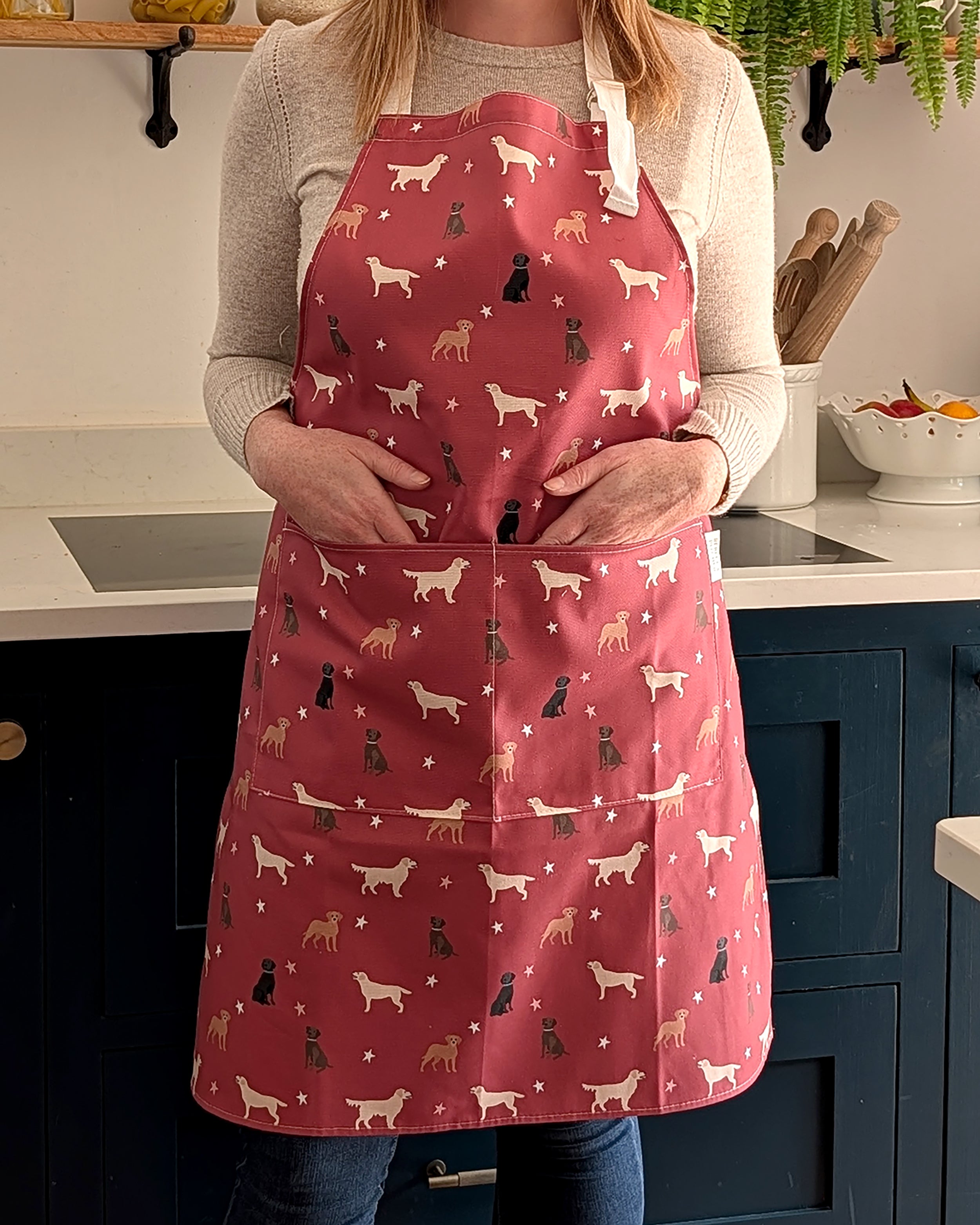 Person wearing a red apron with labrador dog patterns in a kitchen setting