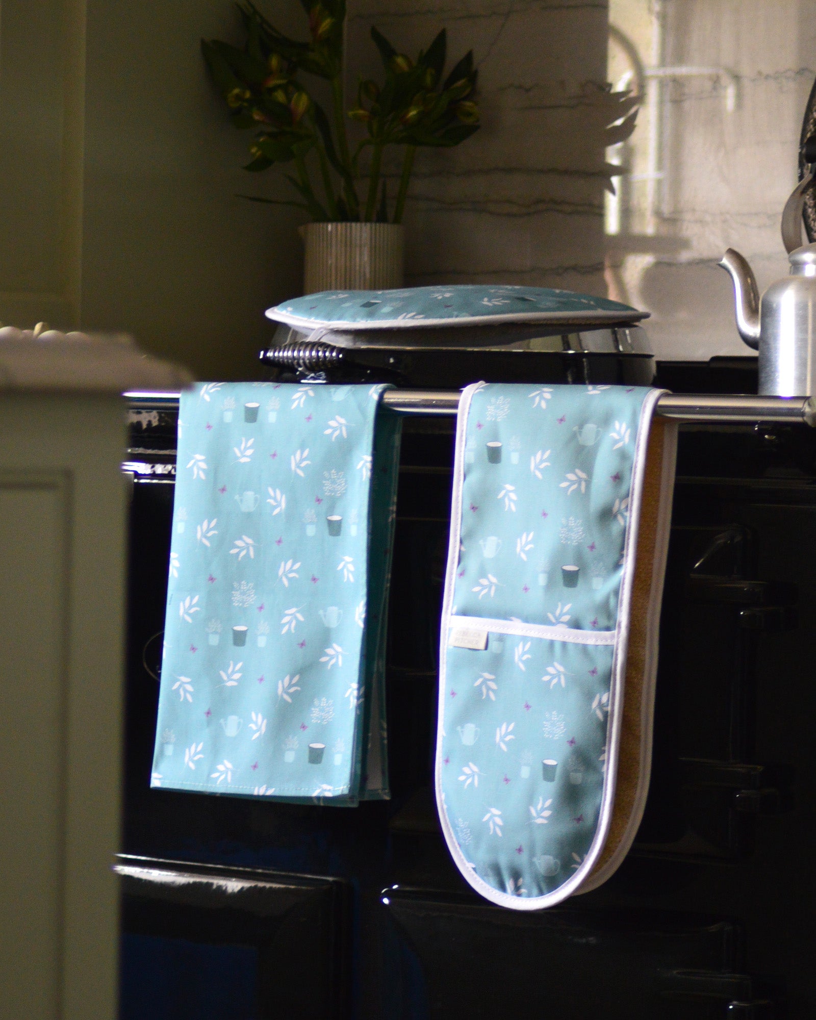 Teal cottage garden patterned oven mitt and tea towel hanging on a stove.