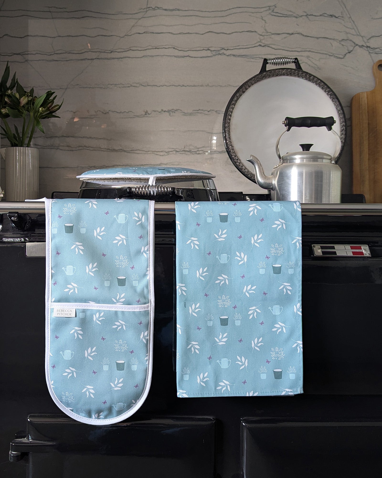 Set of duckegg blue cottage garden patterned oven mitt and tea towel on a kitchen range cooker.