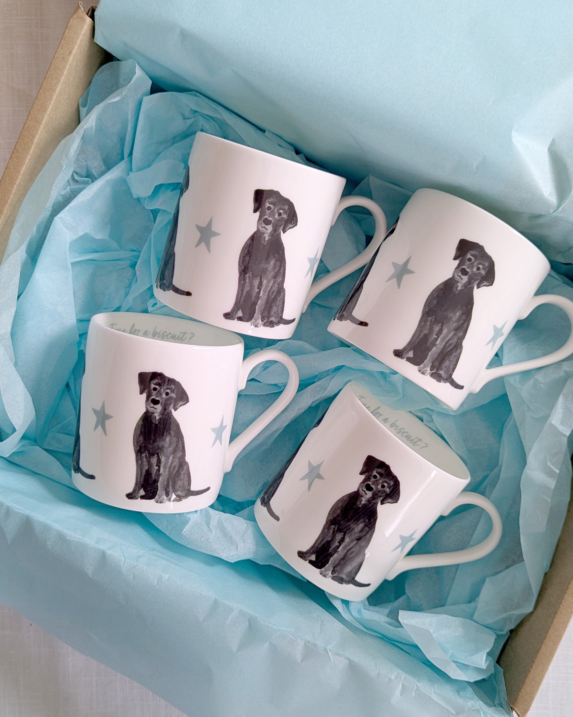Set of four white mugs with black labrador dog illustrations on blue tissue paper