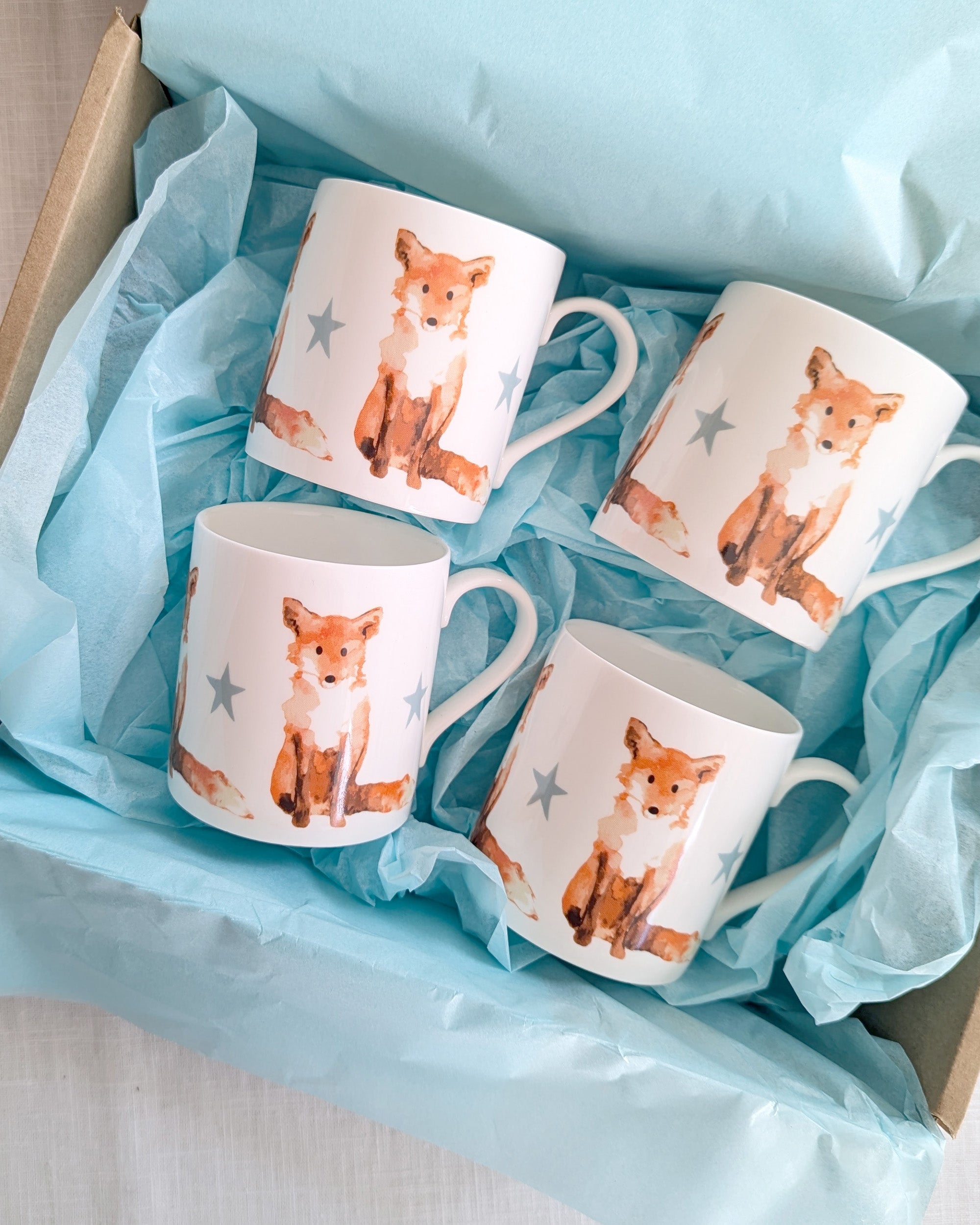 Four mugs with fox illustrations in a box lined with blue tissue paper