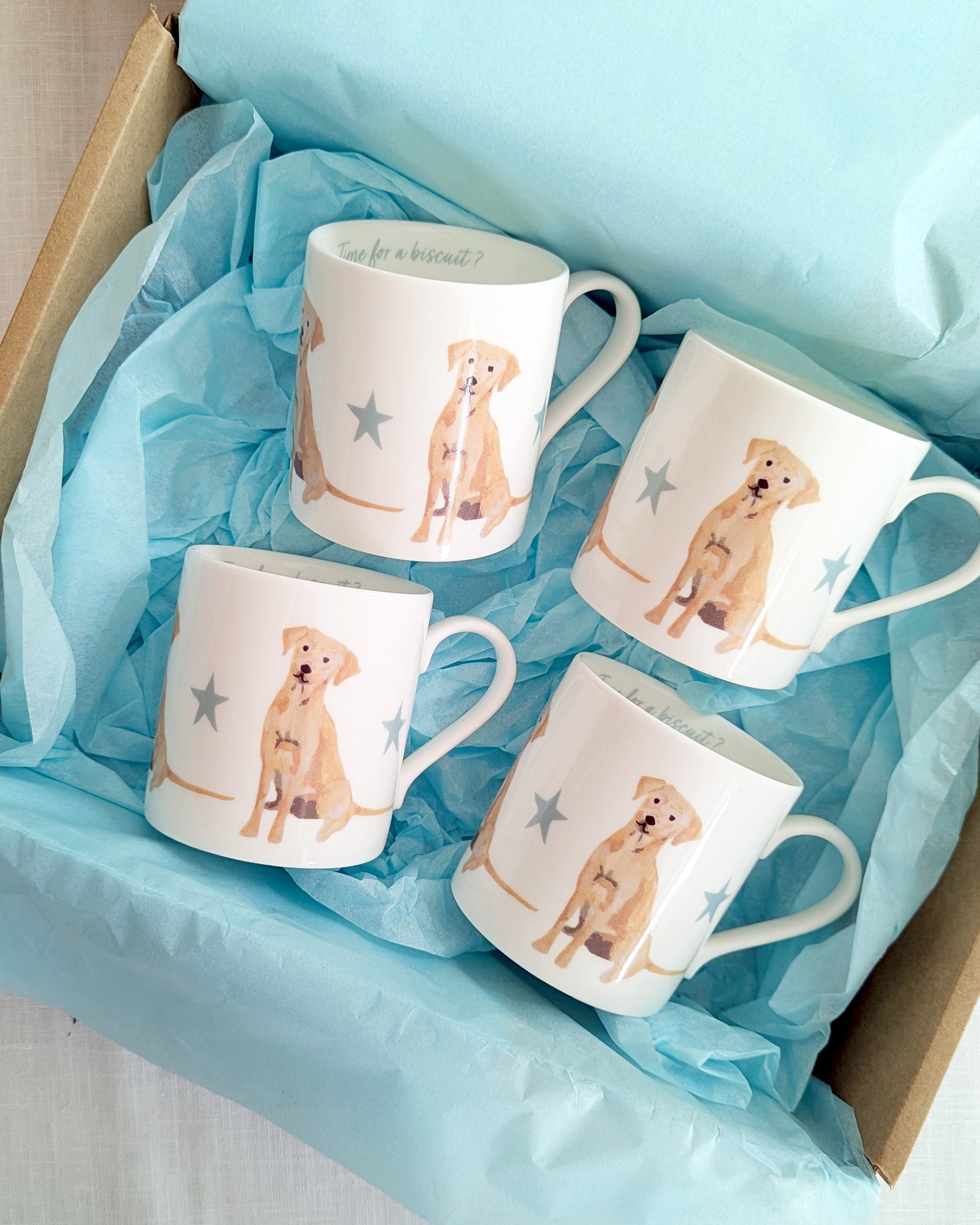 Four mugs with golden labrador dog illustrations on blue tissue inside a box