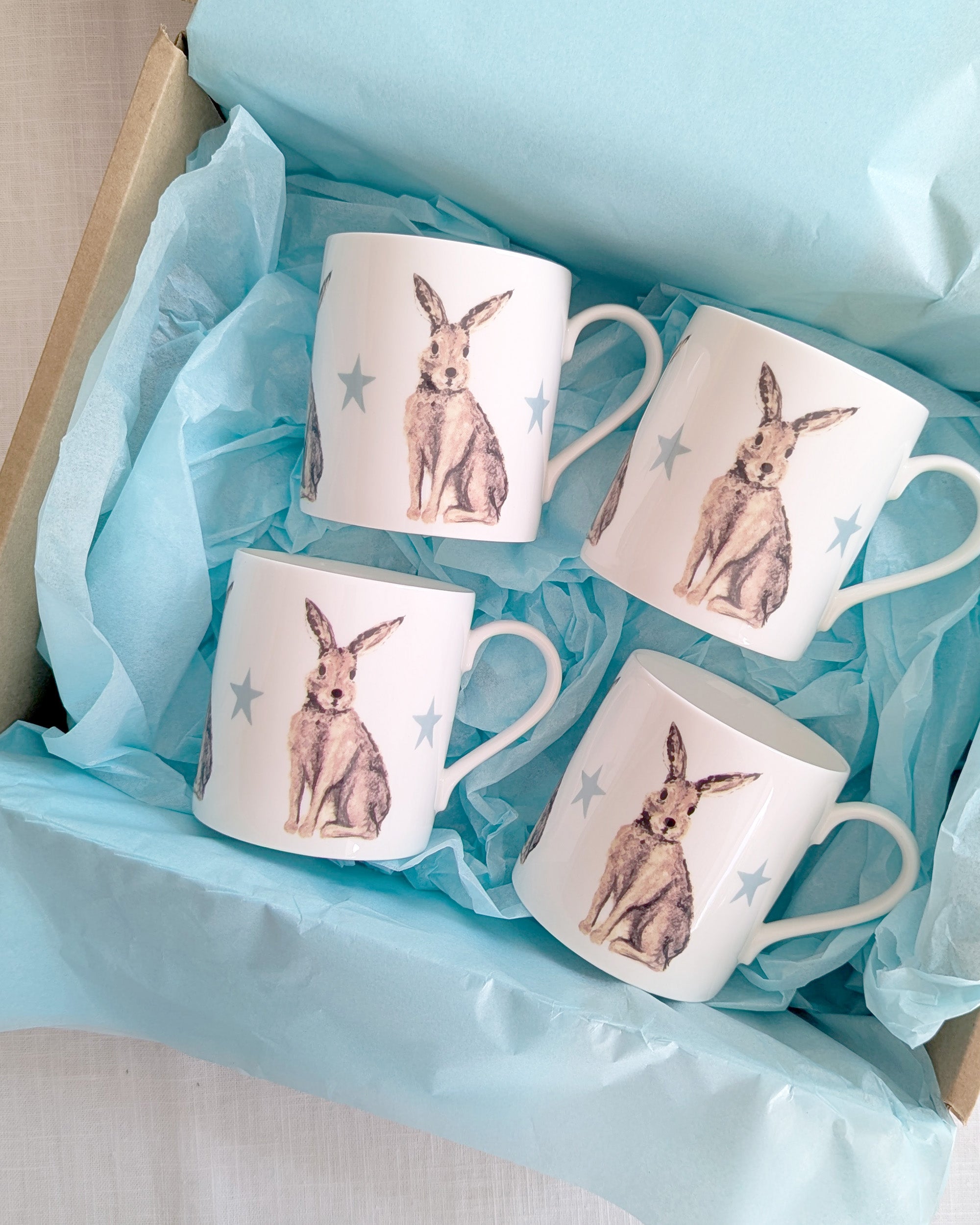 Four mugs with hare illustrations in a box lined with blue tissue paper