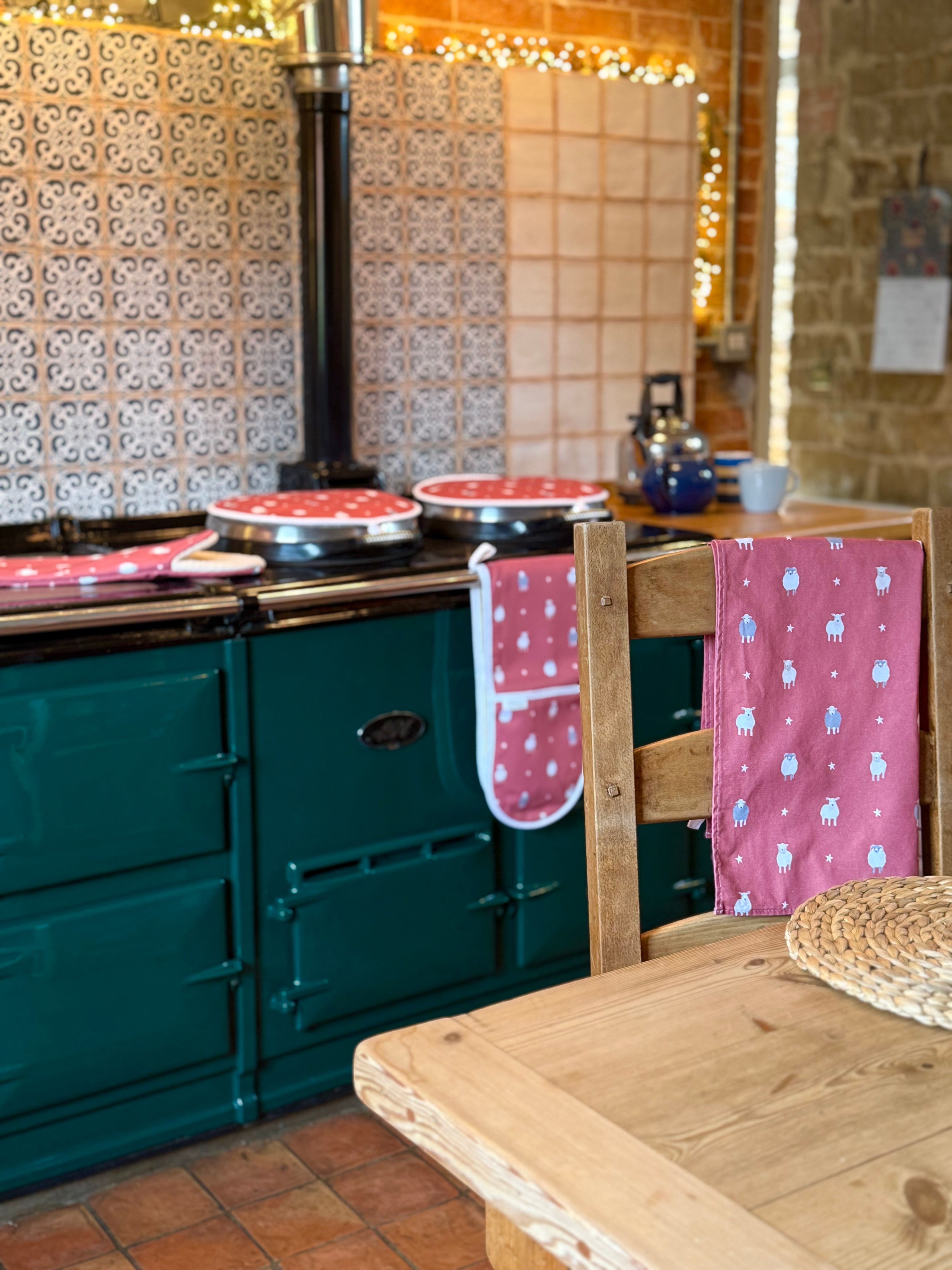 Green Aga range cooker with red sheep kitchen textiles in a rustic kitchen.