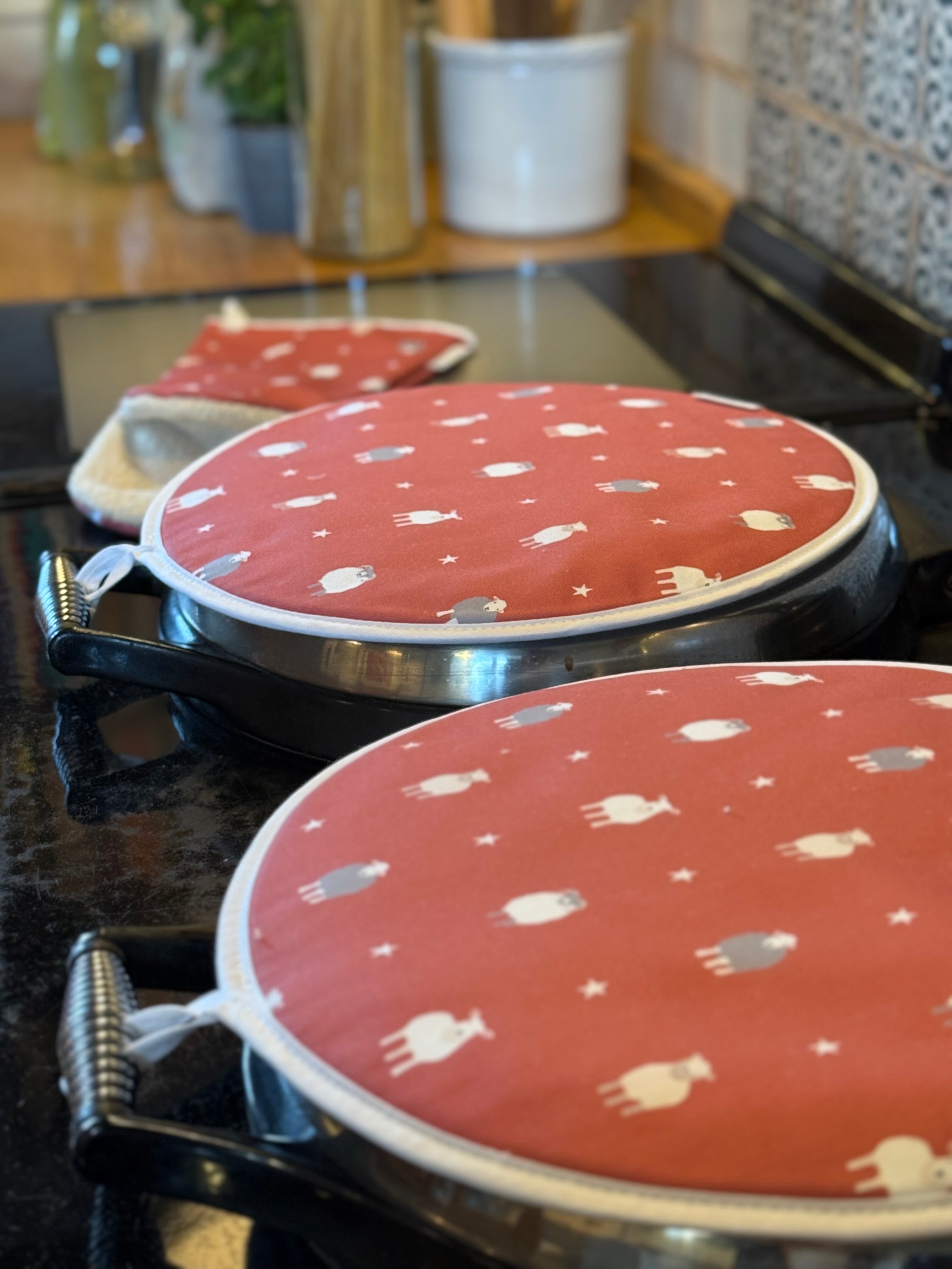 Two red hob pads with white sheep patterns on a stove