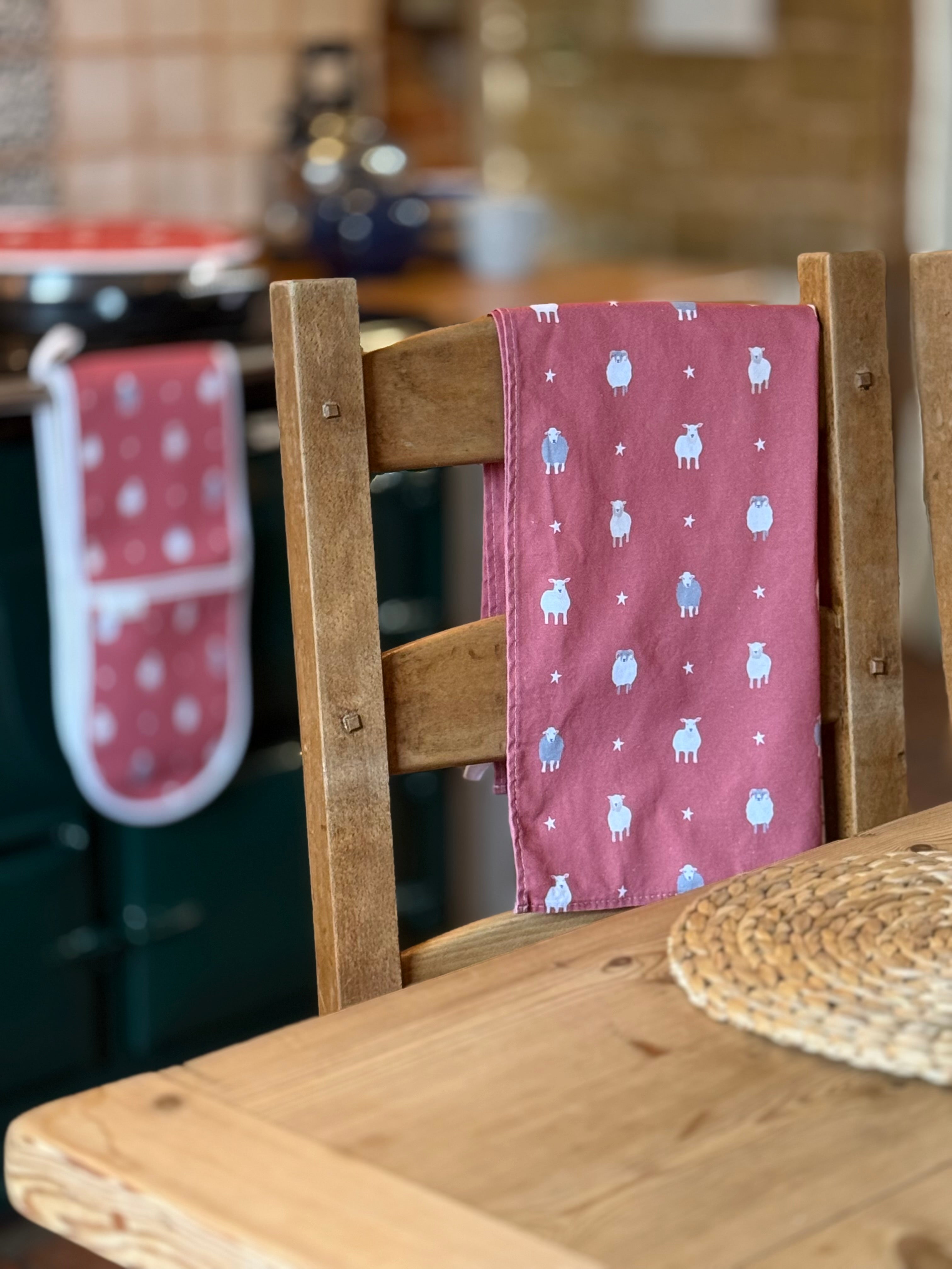 Wooden chair with a red towel featuring sheep designs, hanging on a kitchen counter.