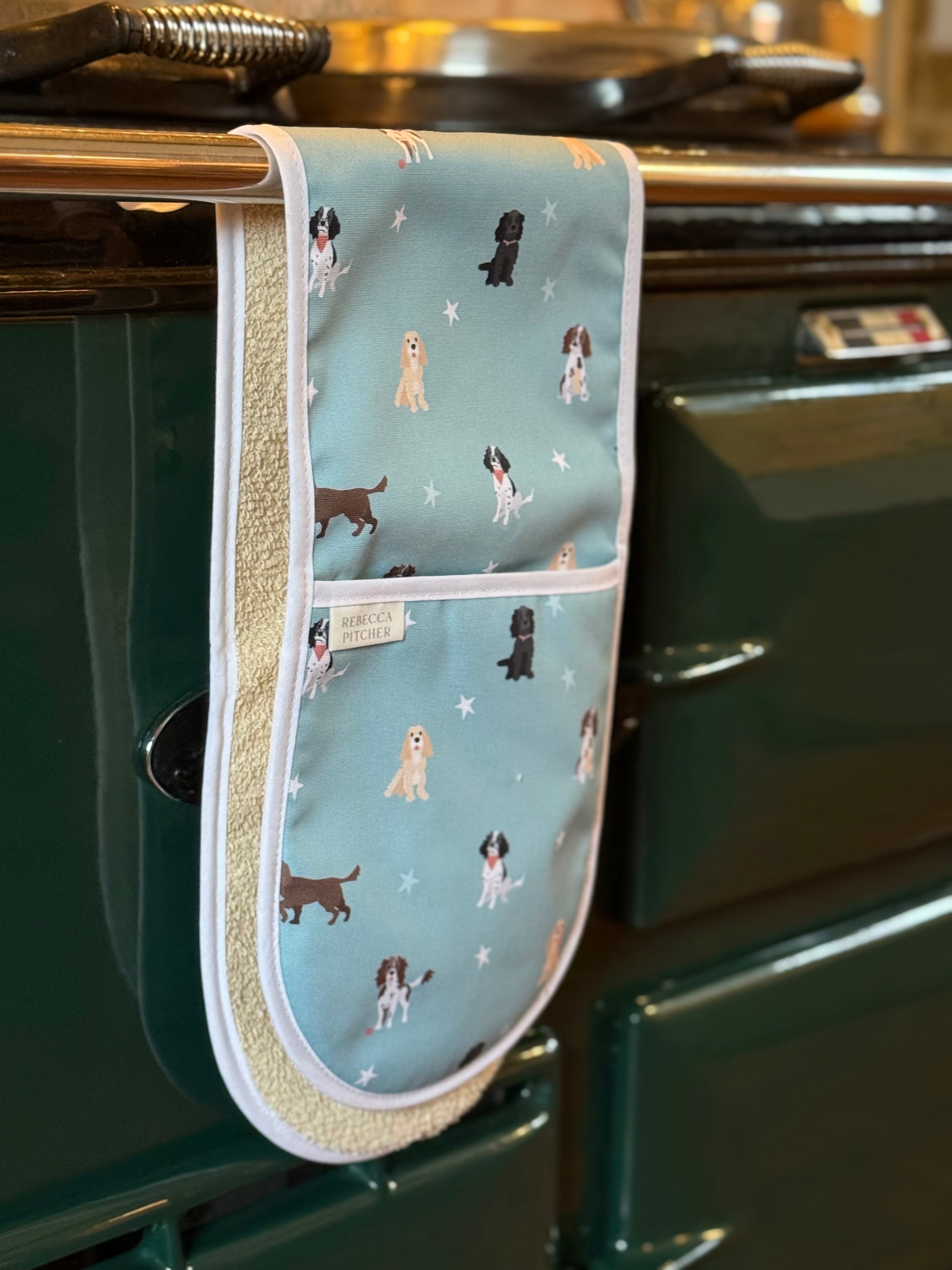 Oven mitt with spaniel dog pattern hanging on a green Aga range cooker.