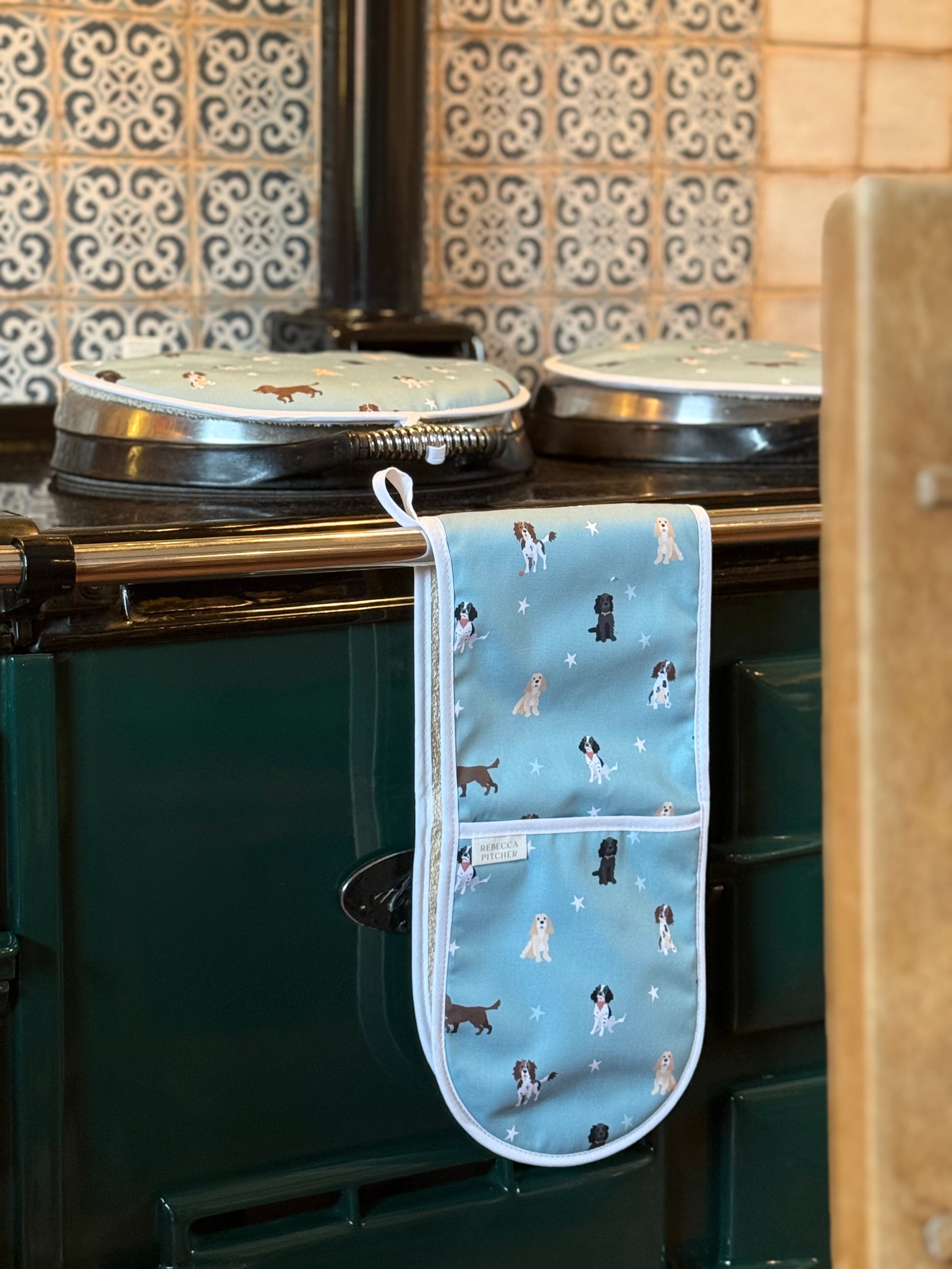 Oven mitt with spaniels dog pattern hanging on a green range cooker.