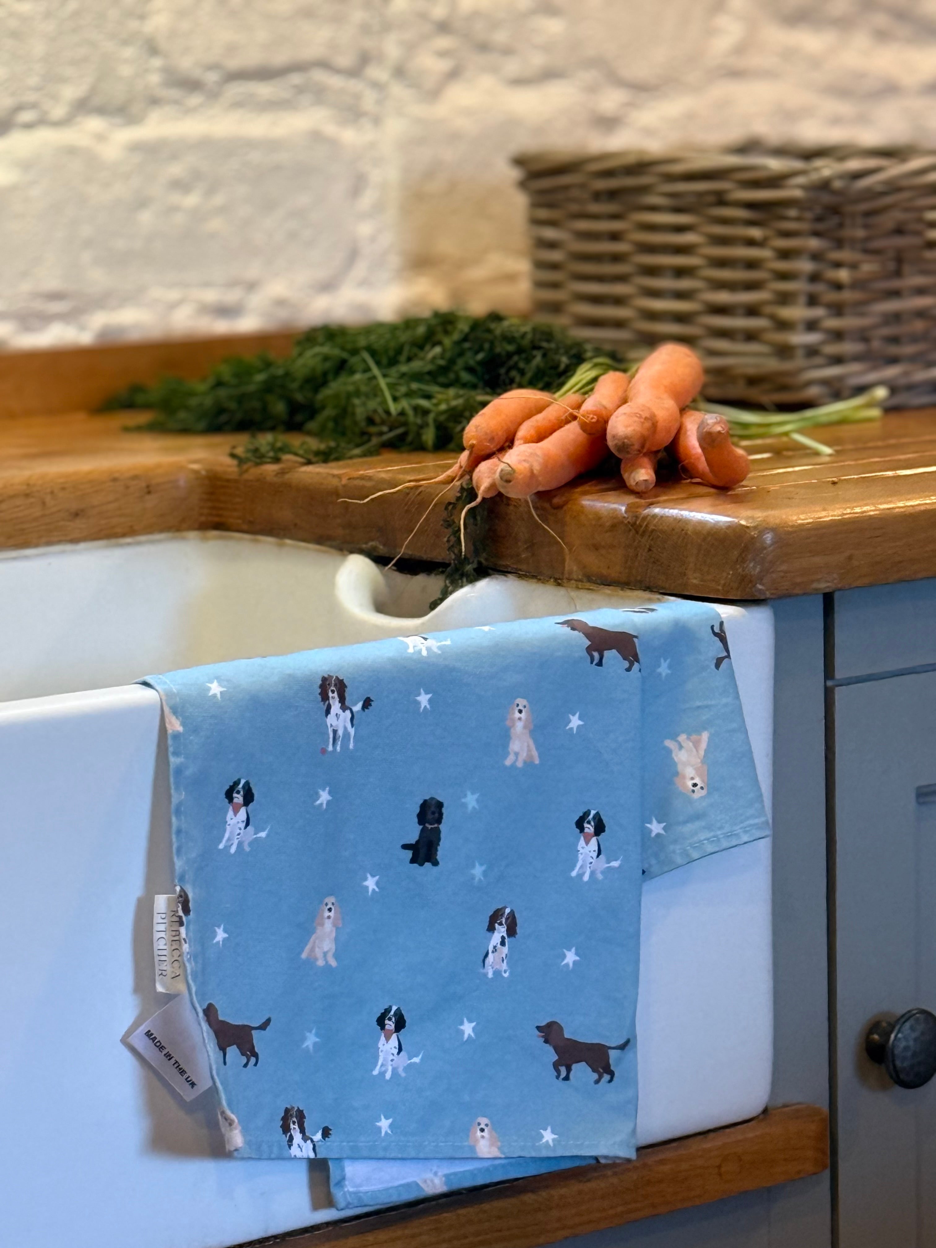 Blue towel with spaniel dog pattern hanging on a kitchen cabinet next to carrots and greens.
